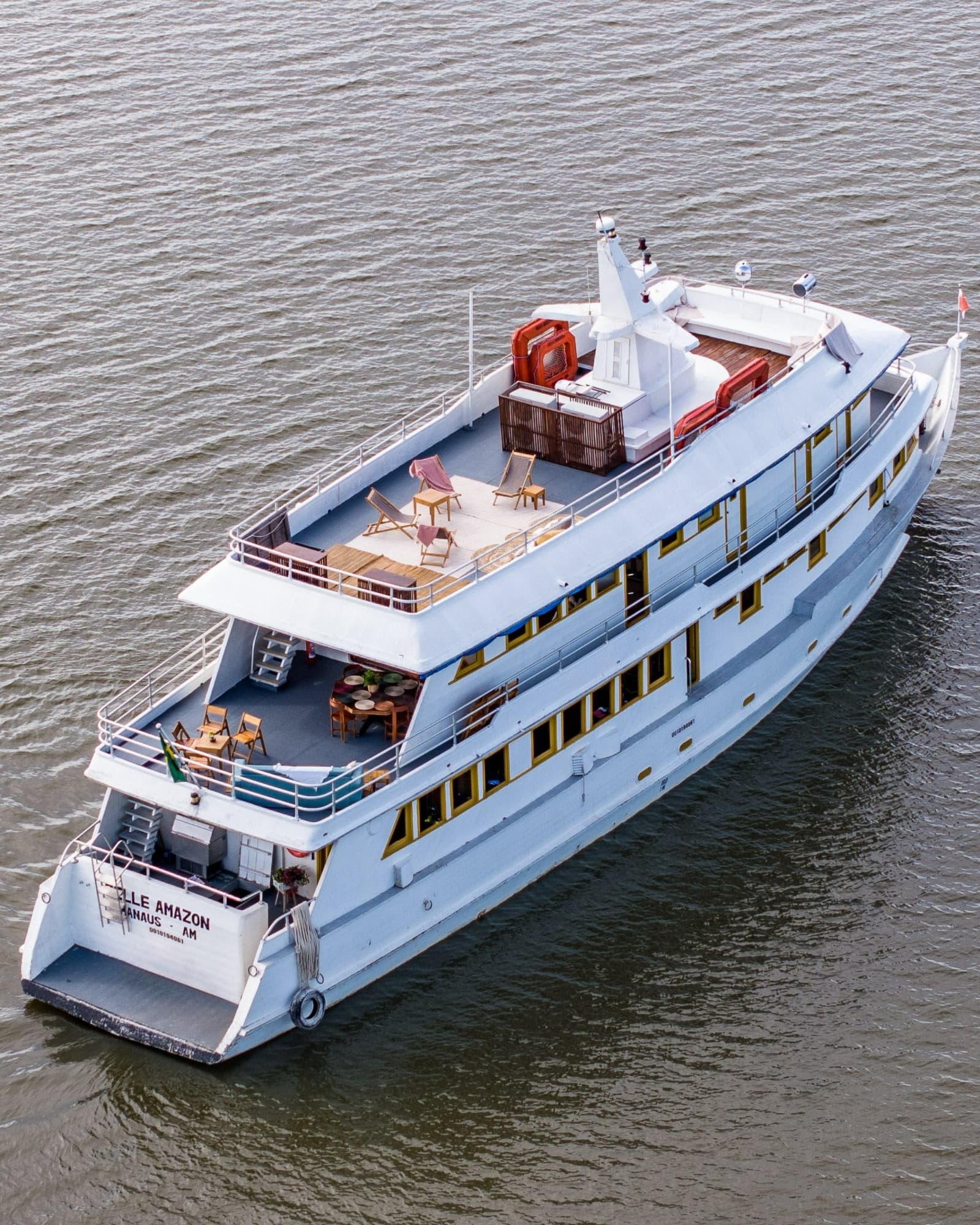 Your home on the river, seen from a bird's perspective. Aerial view of the Belle Amazon river cruise vessel underway on the Amazon River, with open sun decks, deck chairs, and dining furniture visible across three levels