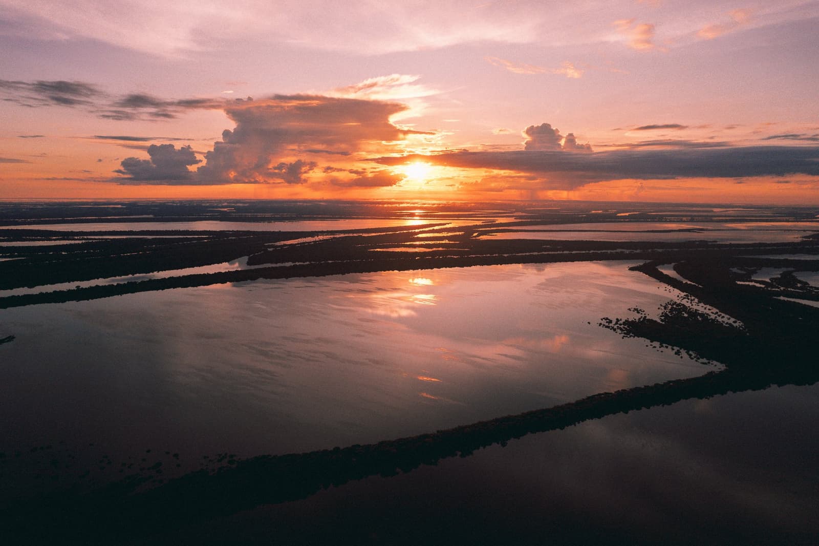 The river keeps every colour the sky is willing to give. Aerial view of a vast flooded Amazonian floodplain at sunset, with orange and pink light reflected across interconnected waterways and dark forested islands, near Anavilhanas Jungle Lodge Brazil