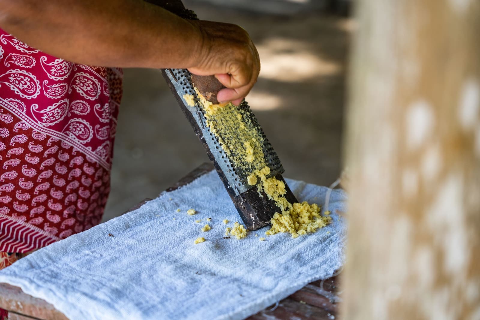 Cassava flour starts here, one rough grate at a time. A local woman in a red patterned apron grating fresh cassava onto a cloth at the Anavilhanas Jungle Lodge Brazil riverside community visit