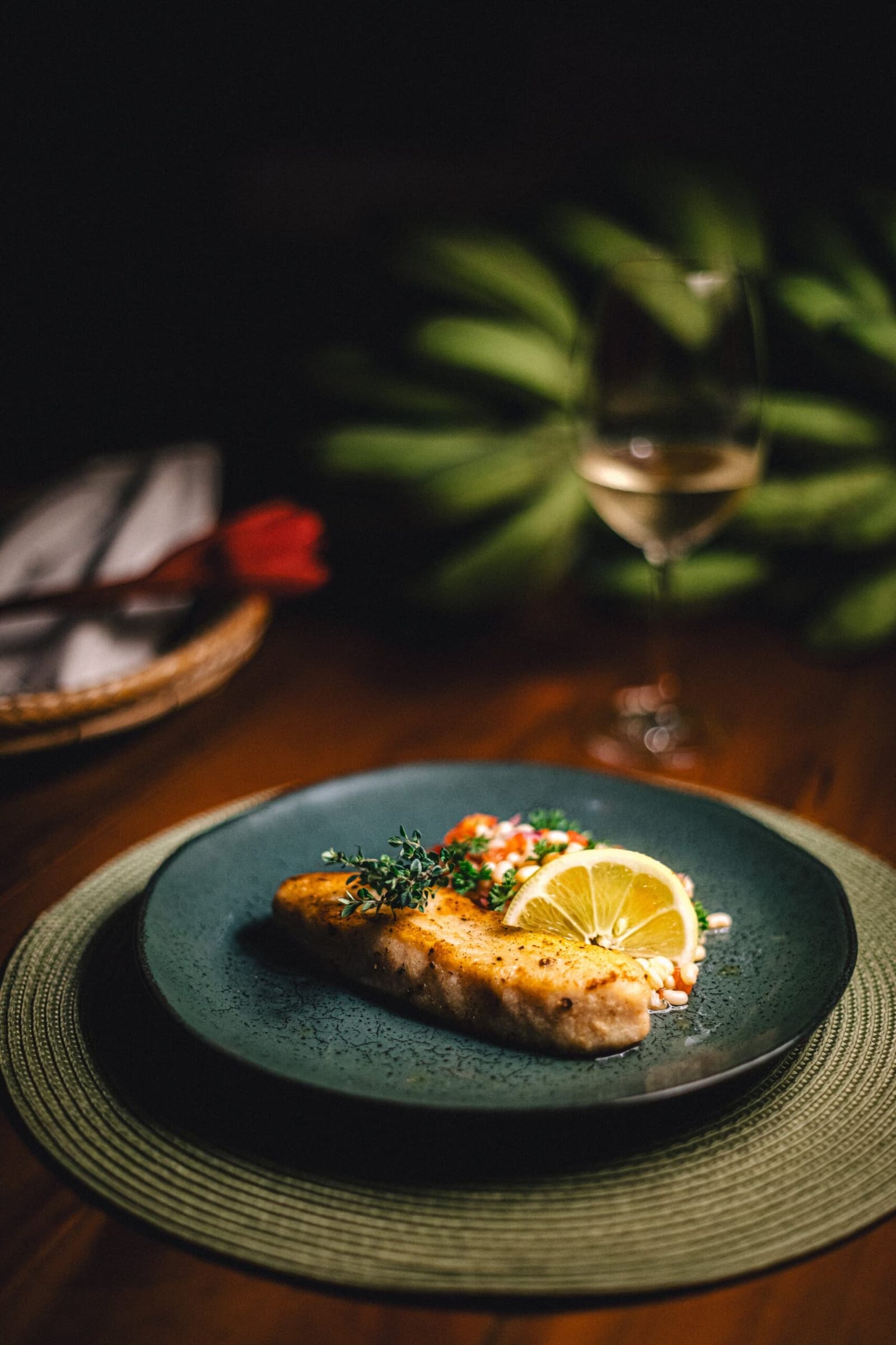 Dinner sorted, and the jungle does the ambiance for free. A pan-seared fish fillet garnished with fresh herbs and a lemon slice on a dark ceramic plate at Anavilhanas Jungle Lodge Brazil, served alongside a glass of white wine
