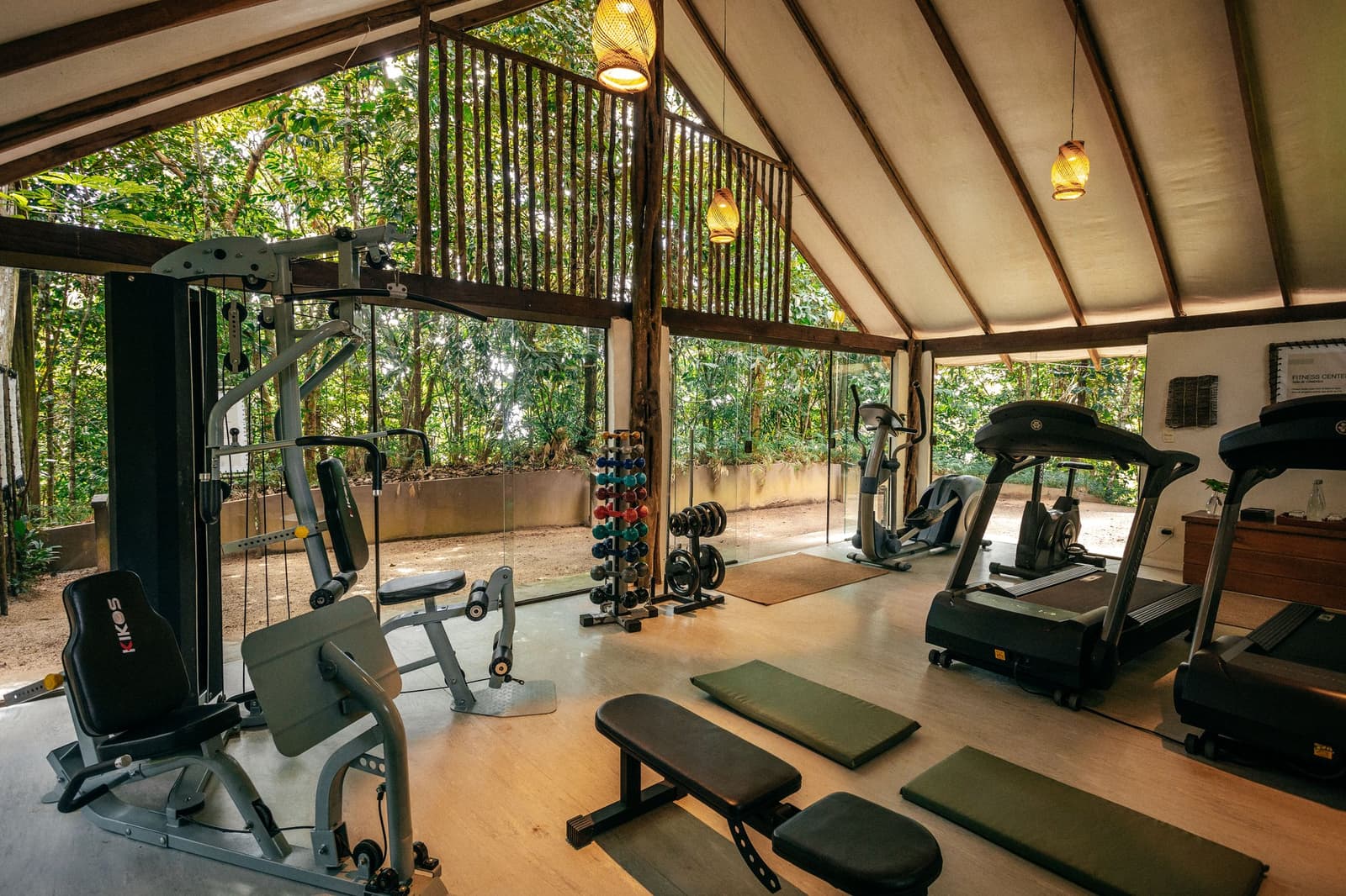 Skip no leg day, even when the Amazon is right outside the window. Open-air fitness center at Anavilhanas Jungle Lodge Brazil, with cable machines, treadmills, free weights and yoga mats beneath a canvas roof, surrounded by lush rainforest through floor-to-ceiling glass walls