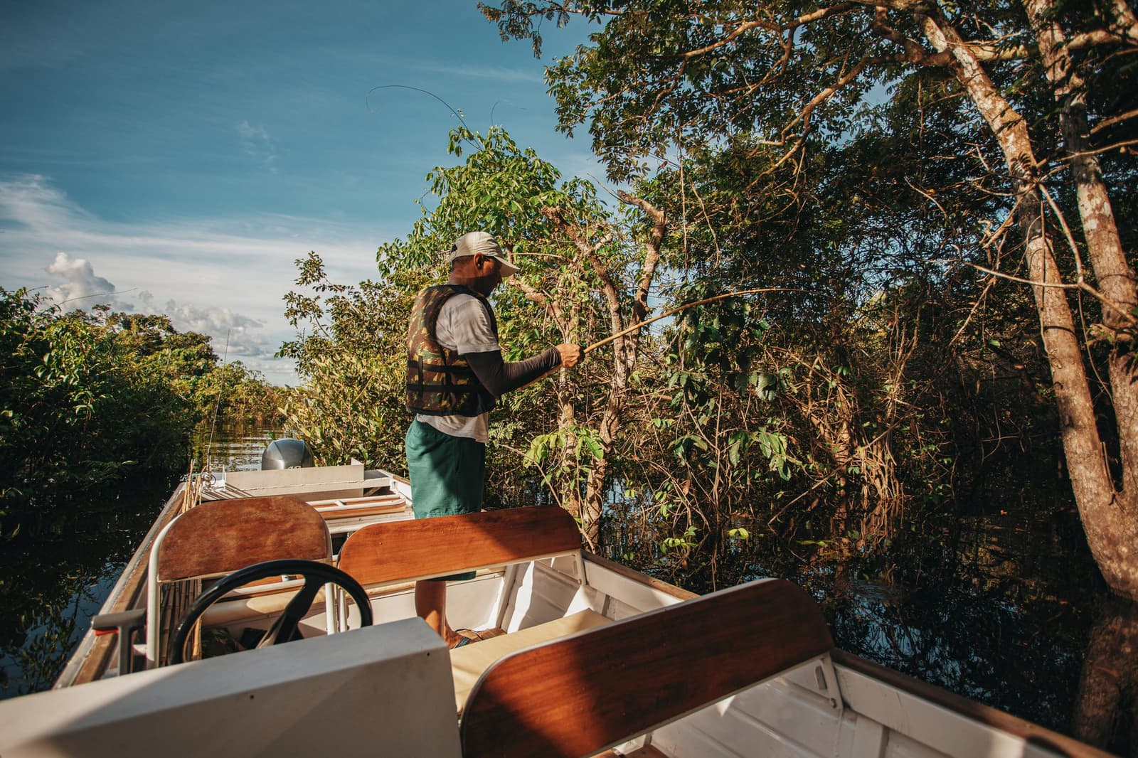 Local knowledge, a bamboo rod, and patience, the Amazon fishes on its own terms. A guide stands at the bow of a small motorboat, fishing rod in hand, casting toward dense riverside vegetation during a recreational fishing excursion at Anavilhanas Jungle Lodge Brazil