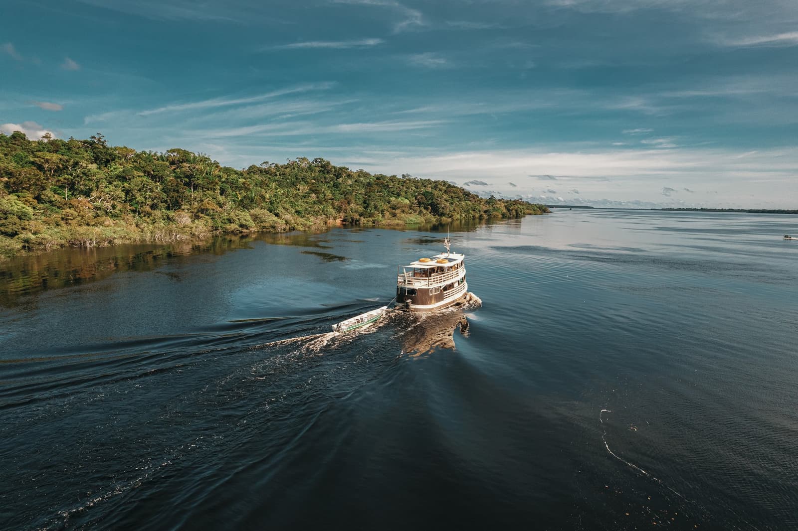 Your floating base camp, already earning its keep on the river. A two-deck wooden expedition boat cruises the dark waters of the Rio Negro past dense Amazon rainforest on a full-day Anavilhanas Jungle Lodge Brazil excursion