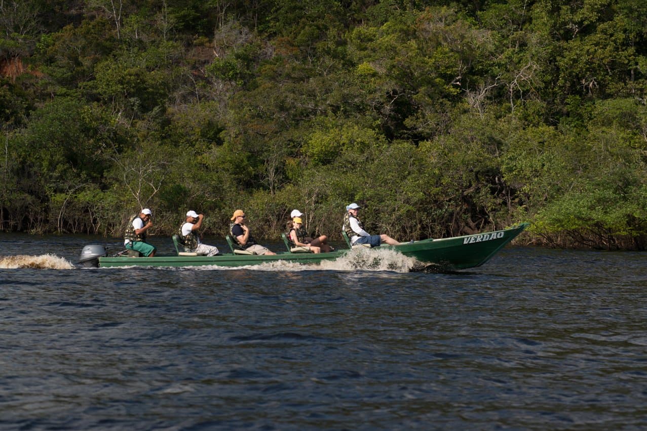 The fastest way to feel how big the Amazon really is. A group of ecotourists in life jackets speeds along the Rio Negro aboard a green motorboat during an Anavilhanas Jungle Lodge Brazil expedition, with dense riparian forest lining the far bank