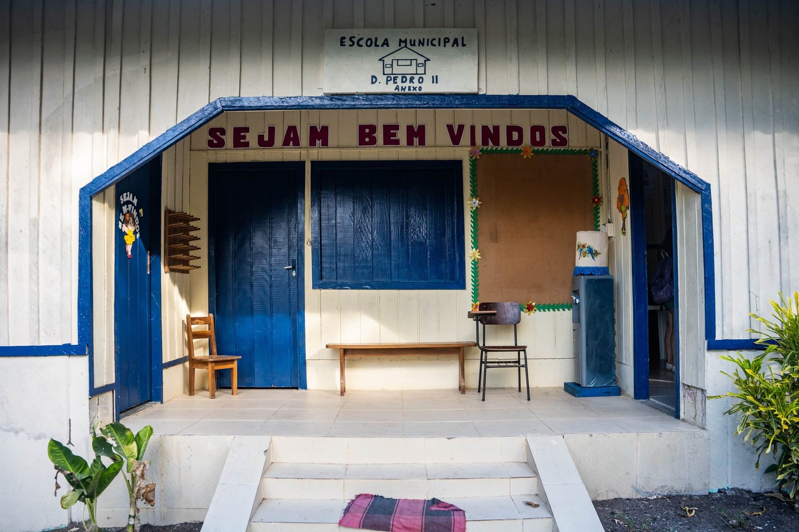 The welcome sign means it: this little school takes its job seriously. Entrance of Escola Municipal D. Pedro II, a white wooden community school with blue trim and a 'Sejam Bem Vindos' welcome sign, visited during an Anavilhanas Jungle Lodge Brazil riverside community excursion