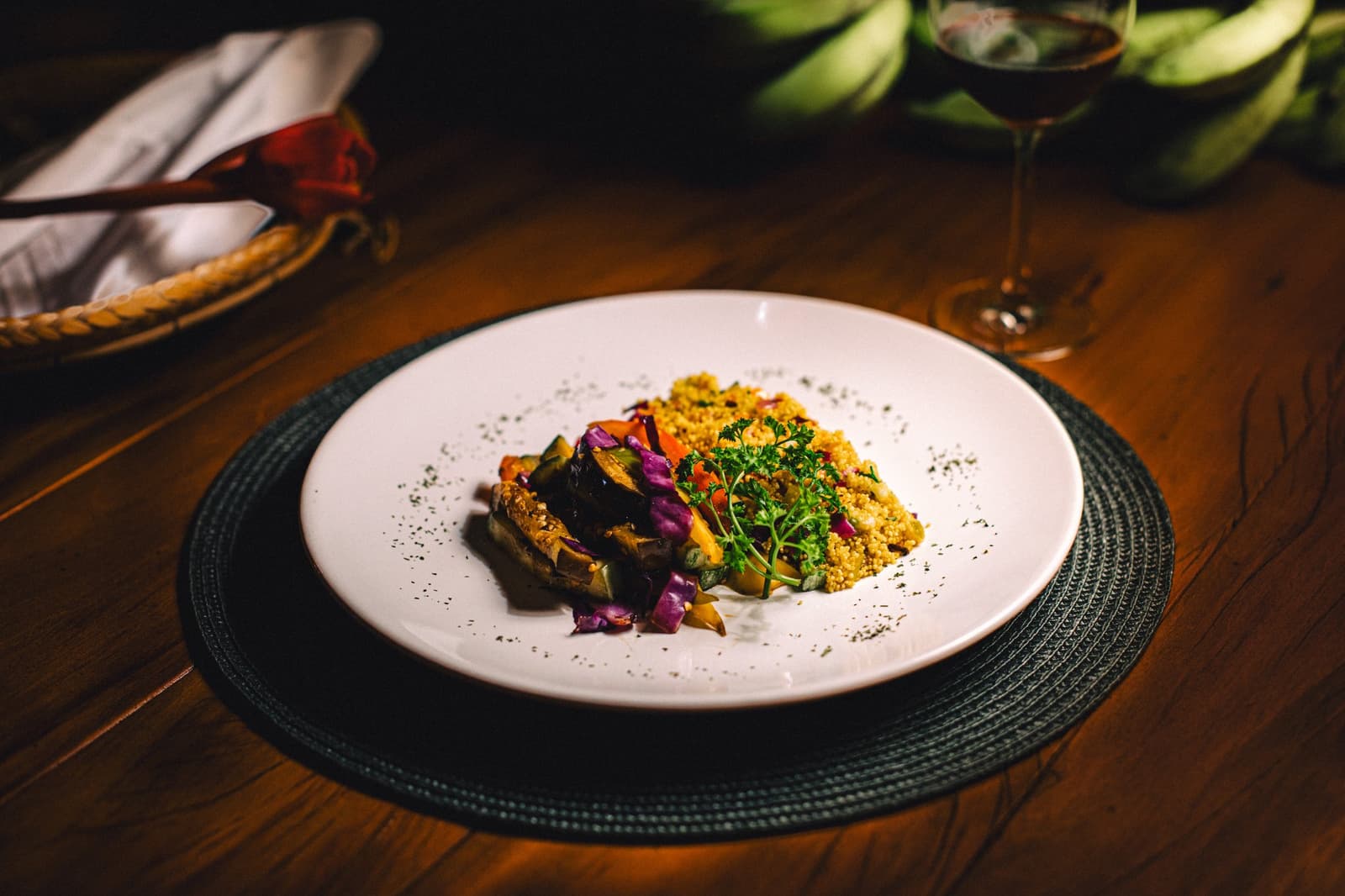 Good food and a glass of red wine, the Amazon night starts well. A plated dinner at Anavilhanas Jungle Lodge Brazil featuring roasted vegetables, golden couscous and fresh herbs on a white dish, with a glass of red wine in the background