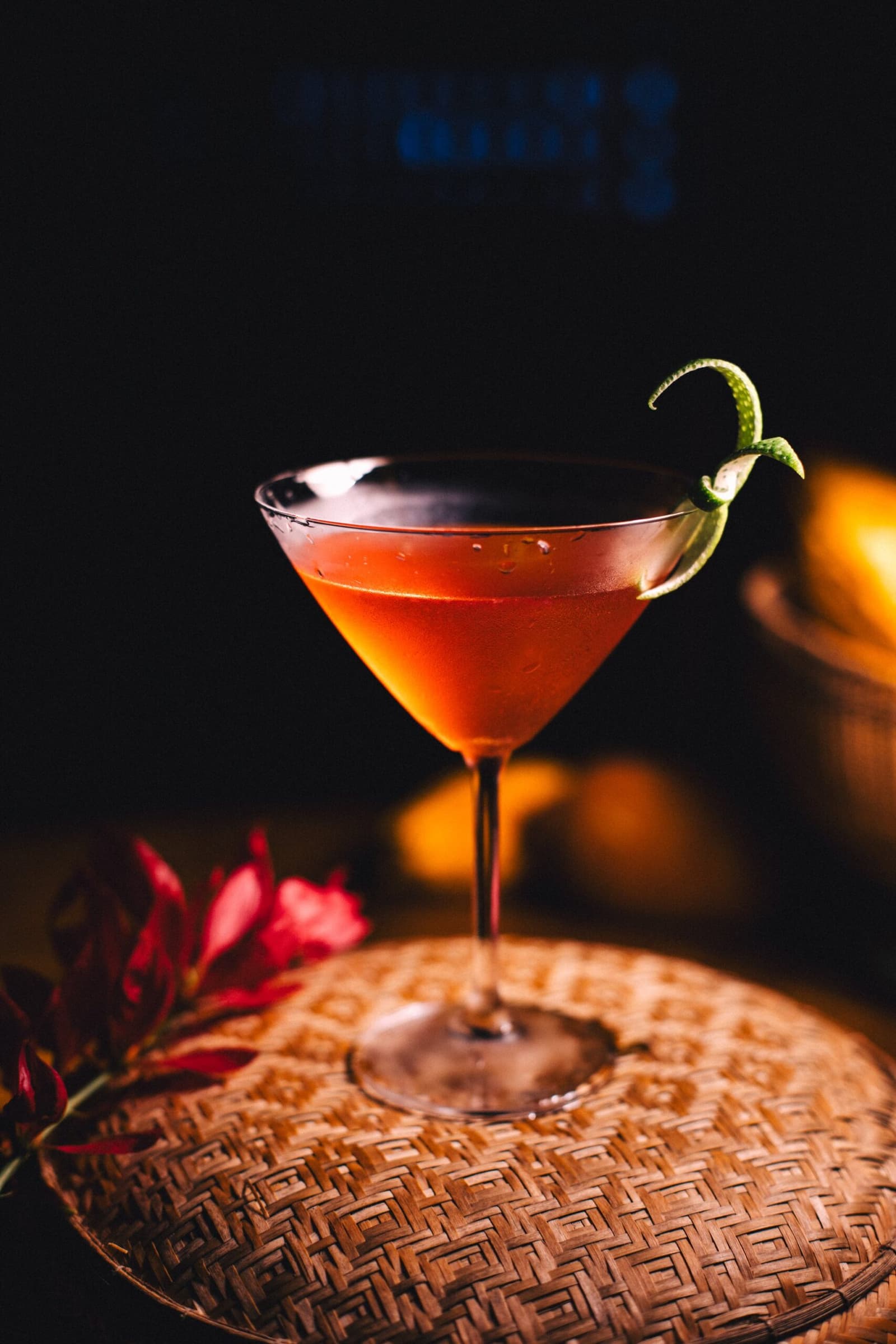 The jungle has a way of making happy hour feel earned. A deep red cocktail in a martini glass garnished with a lime twist, resting on a woven tray beside a red tropical flower at Anavilhanas Jungle Lodge Brazil
