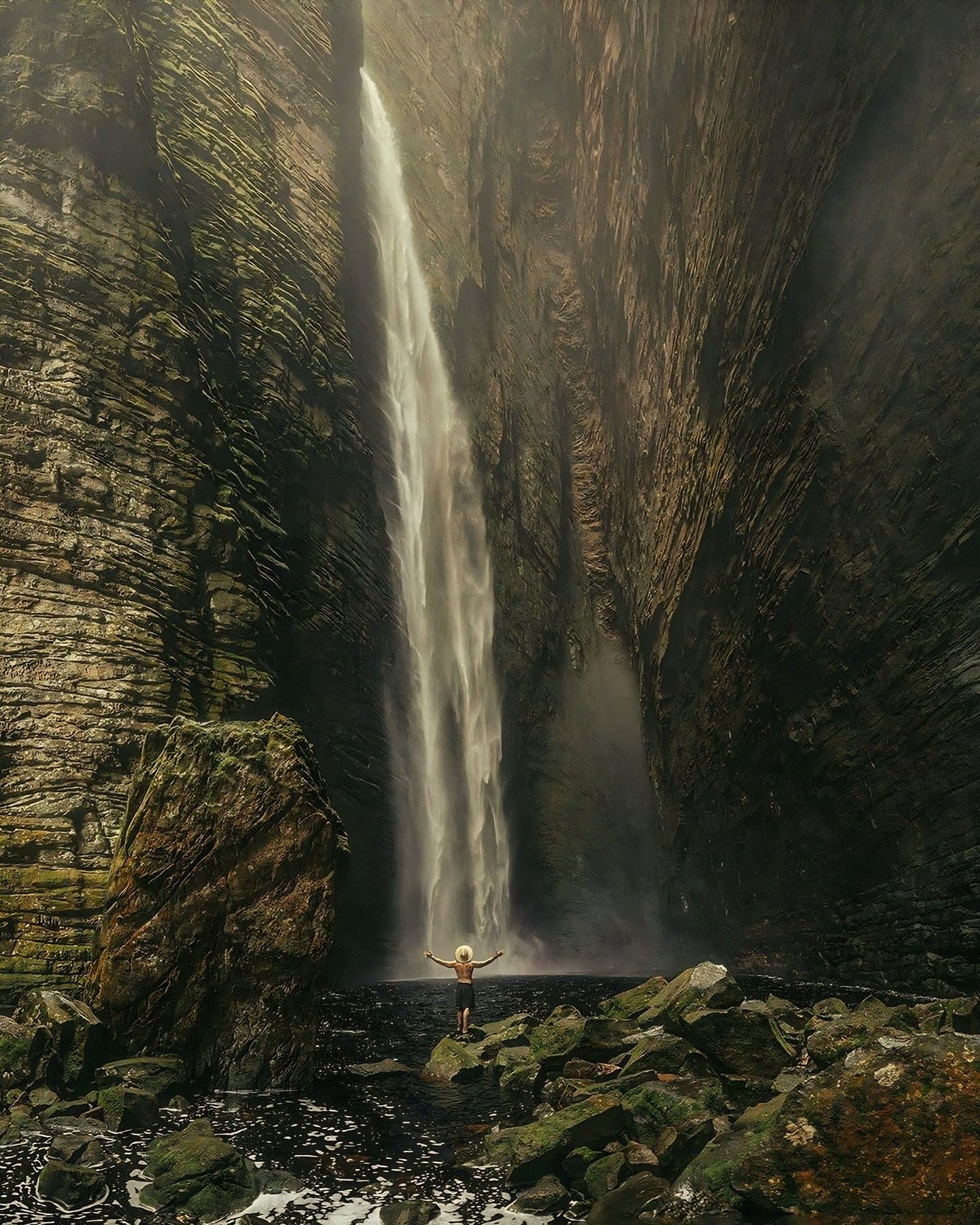 That moment when the canyon puts your ego in perspective. A lone hiker stands with arms raised before the towering Fumacinha waterfall plunging through a narrow sandstone canyon on a Chapada Diamantina hike