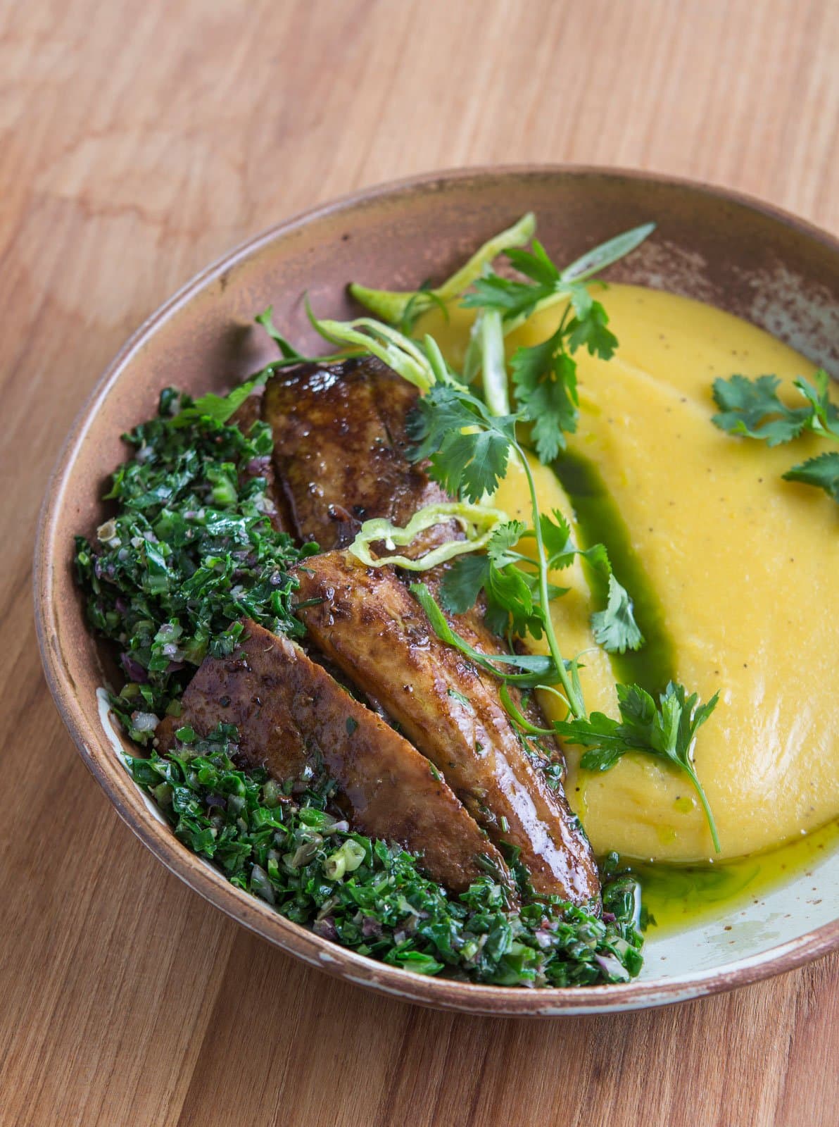 Lodge cooking that takes the rainforest pantry seriously. A rustic ceramic bowl at Cristalino Jungle Lodge holding caramelised plantain slices, vibrant herb salsa, and a smooth golden purée garnished with fresh coriander