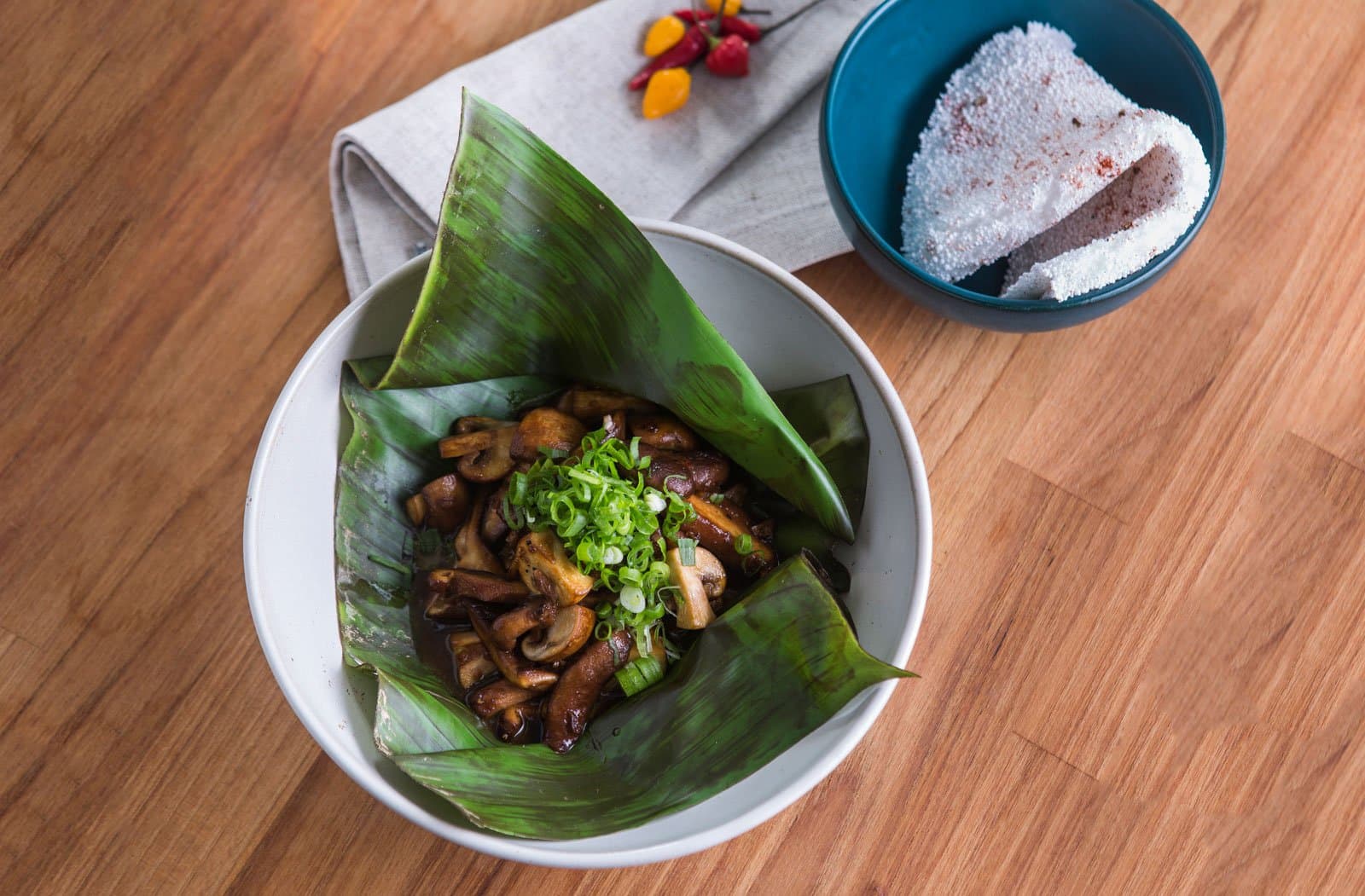 Forest flavors, plated with more care than you might expect this deep in the Amazon. Sautéed mushrooms garnished with sliced spring onions, served in a banana leaf inside a white ceramic bowl at Cristalino Jungle Lodge, with a side of cassava flatbread dusted in red spice and small chilli peppers on a linen napkin