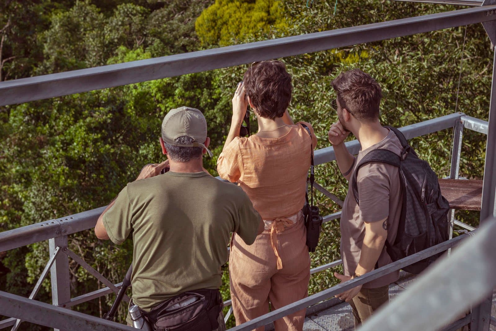 All eyes on the treetops, the canopy always has something to say. Three visitors scan the rainforest canopy with binoculars from a steel observation tower at Cristalino Jungle Lodge