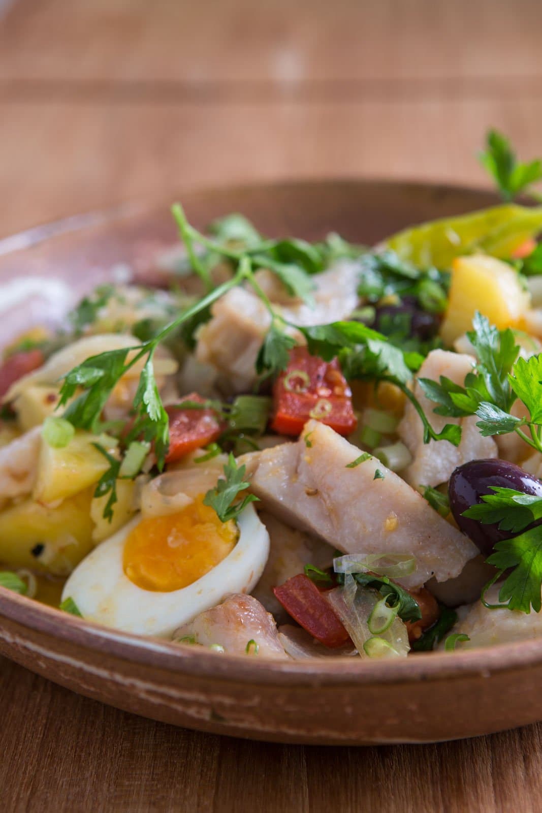 Comfort food with a Portuguese soul, eaten deep in the Amazon. A rustic clay bowl filled with flaked white fish, boiled egg halves, diced yellow potato, black olives, chopped red sausage, spring onion and fresh parsley — a hearty lodge meal at Cristalino Jungle Lodge