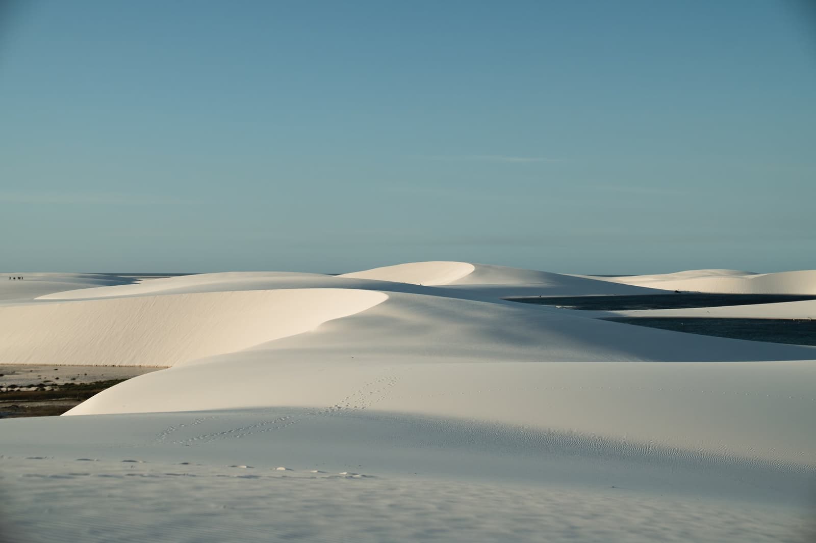 Miles of white sand, a scattering of lagoons, and one set of footprints ahead of yours. Sweeping white sand dunes of Lençóis Maranhenses stretch to the horizon beneath a clear blue sky, with shallow lagoons visible between the sculpted ridges on the horseback riding Lençóis Maranhenses tour route