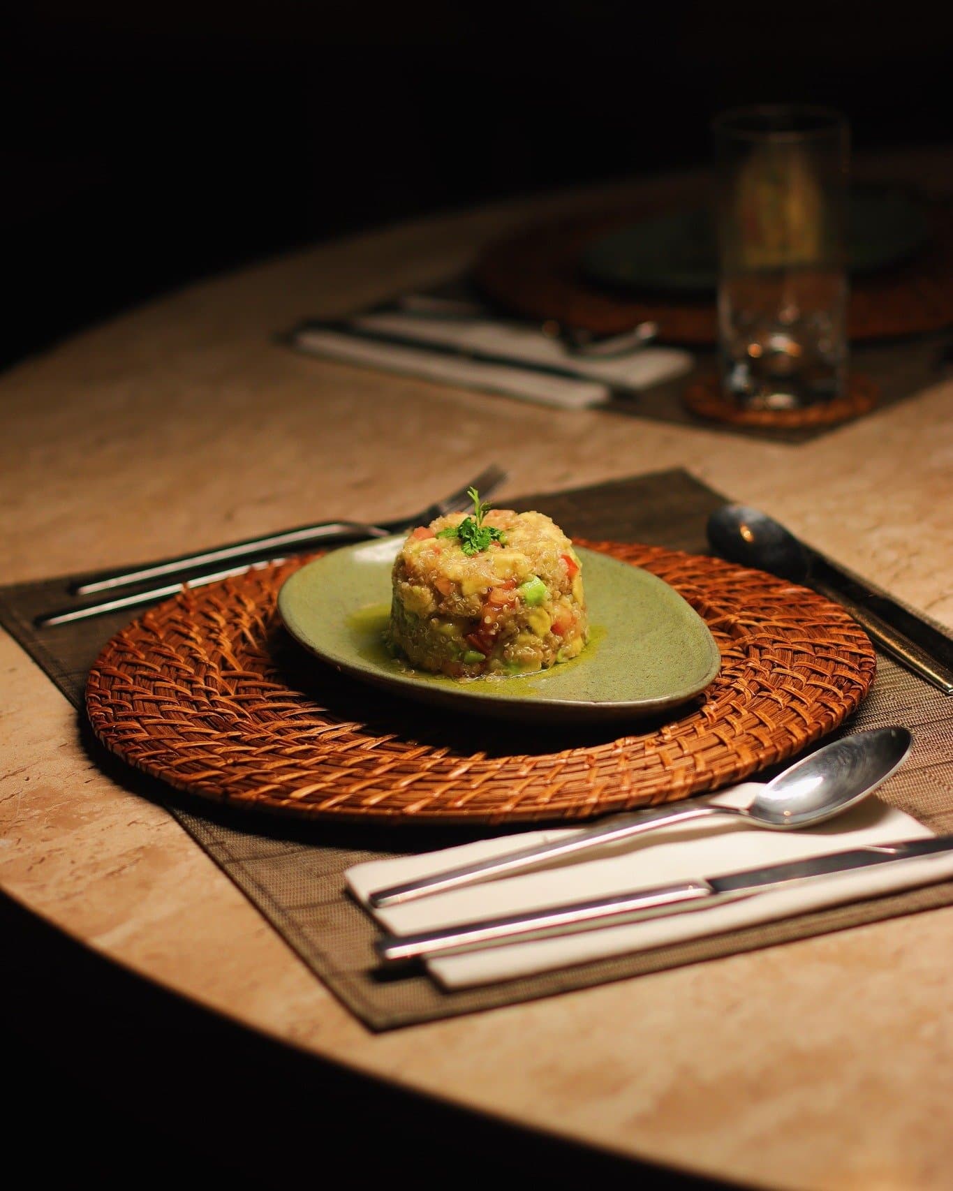 Fine dining finds its way deep into the Amazon, no compromise required. A moulded grain and vegetable dish garnished with fresh herbs, served on a green ceramic plate atop a woven rattan charger at Juma Amazon Jungle Lodge