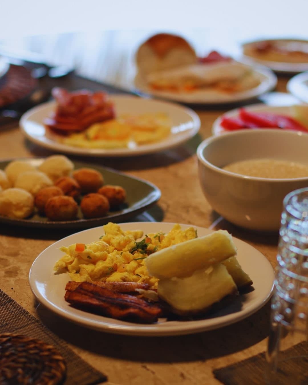 Fuel up before the forest has other plans for your morning. A generous breakfast spread at Juma Amazon Jungle Lodge, with scrambled eggs, crispy bacon strips, boiled cassava, cured meats, fresh red pepper, fried snacks, rolls and a bowl of porridge arranged across a wooden table