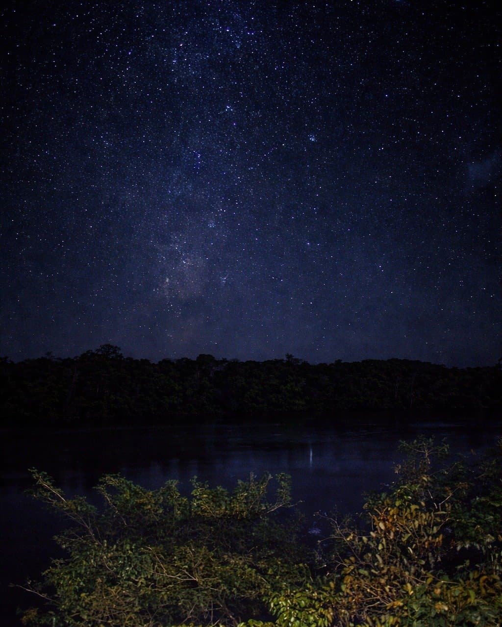 No light pollution, no distractions, just the full weight of the southern sky. The Milky Way stretches across a star-filled sky above a dark jungle river at Juma Amazon Jungle Lodge, with the galactic core faintly reflected in the still water below
