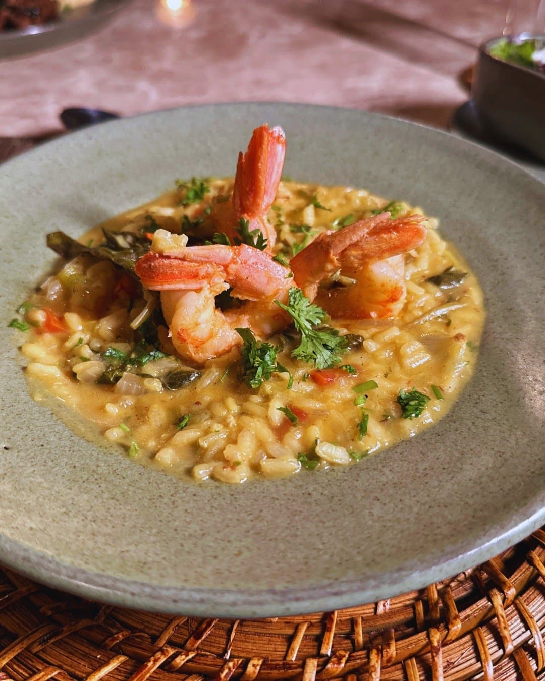 Comfort food gets a rainforest upgrade, whole prawns and all. A bowl of creamy shrimp risotto garnished with fresh herbs, served at Juma Amazon Jungle Lodge on a woven rattan placemat by candlelight