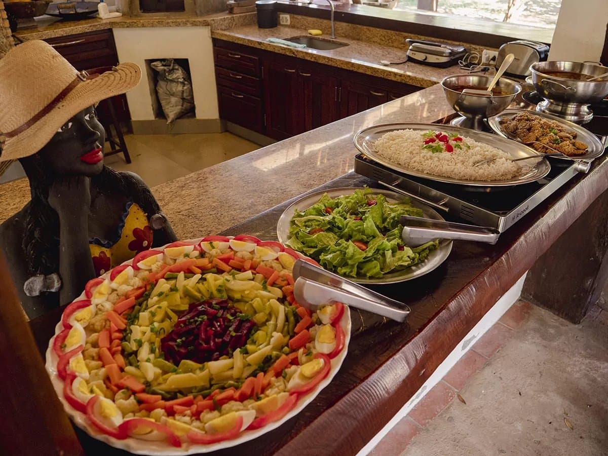 Good food is part of the expedition, not an afterthought. A colorful lodge buffet on a Pantanal Bonito tour featuring a decorative salad platter with boiled eggs, carrots and beetroot, alongside rice, green salad and breaded dishes on a granite counter, with a traditional ceramic figure nearby