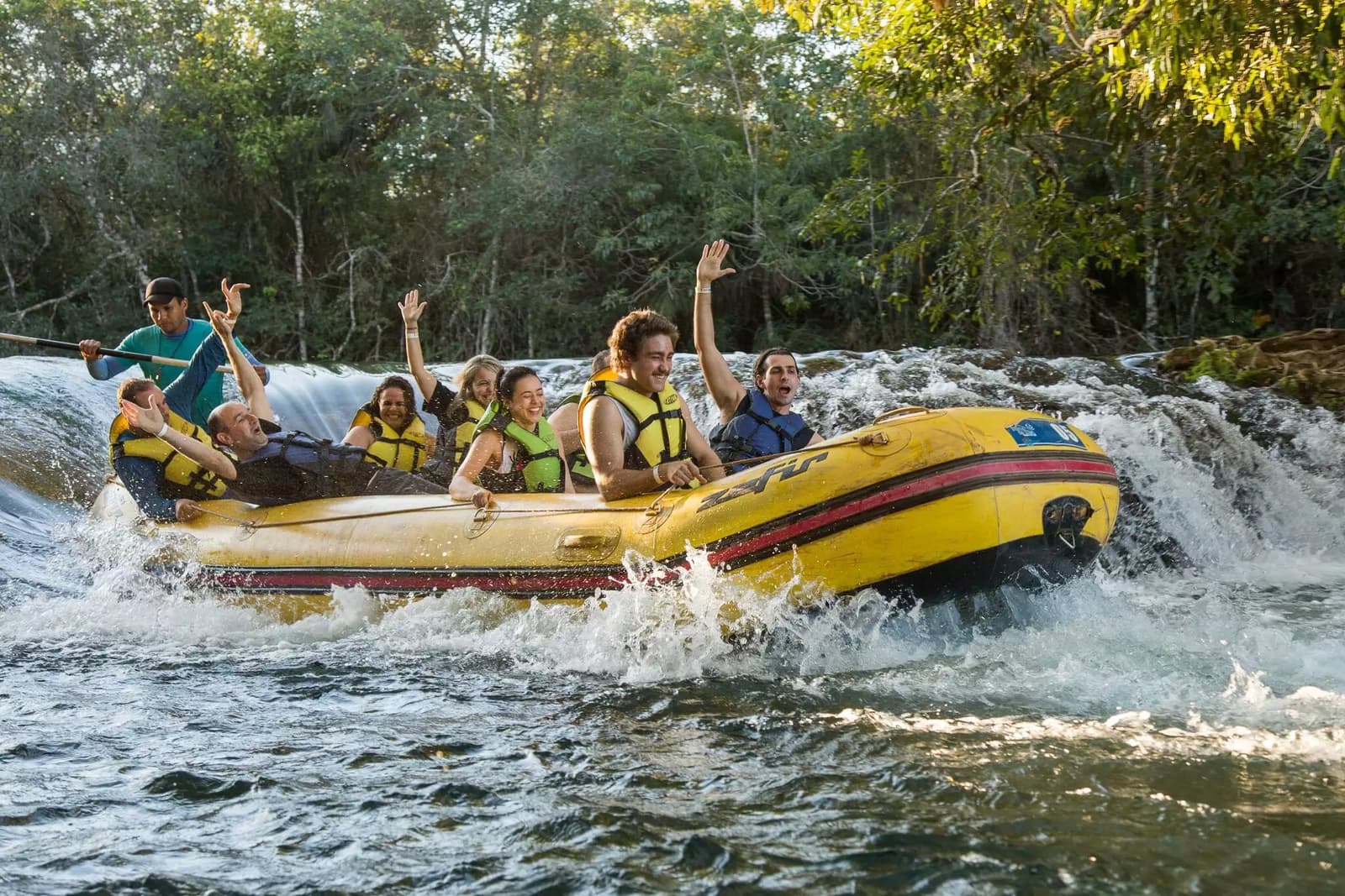 Hands up if you forgot to worry about anything for a solid five seconds. A group of cheering guests in life jackets ride a yellow inflatable raft through churning white-water rapids on a Pantanal Bonito tour, surrounded by lush riverside forest