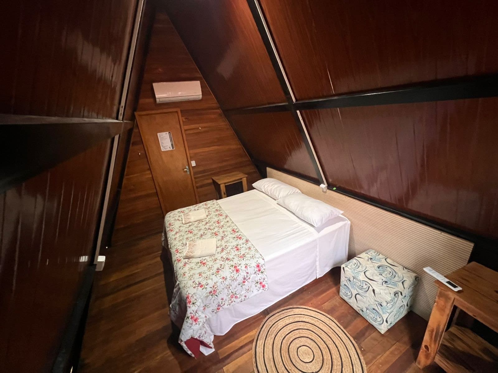 Cozy and clean, with just enough charm to make the jungle feel like home. Interior of an A-frame wooden cabin with a double bed, floral bedspread, timber floors, and air conditioning, offered on a pantanal jaguar budget safari