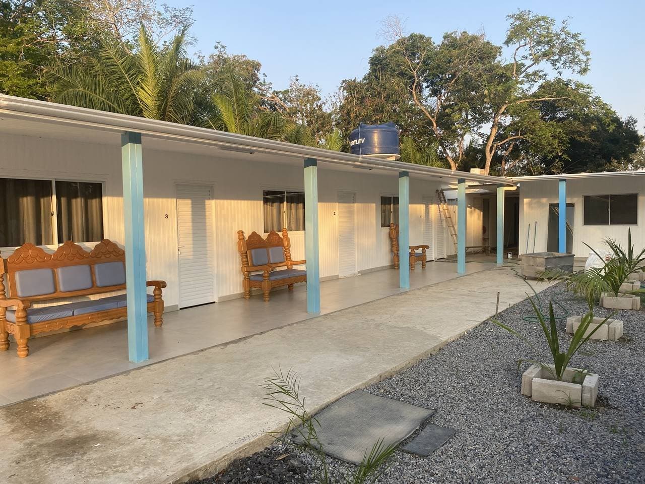 Carved benches, your own door, and the forest right behind. Simple done right. A row of numbered guest rooms with carved wooden benches on a covered verandah, surrounded by tropical trees â simple, comfortable accommodation on a pantanal jaguar budget safari