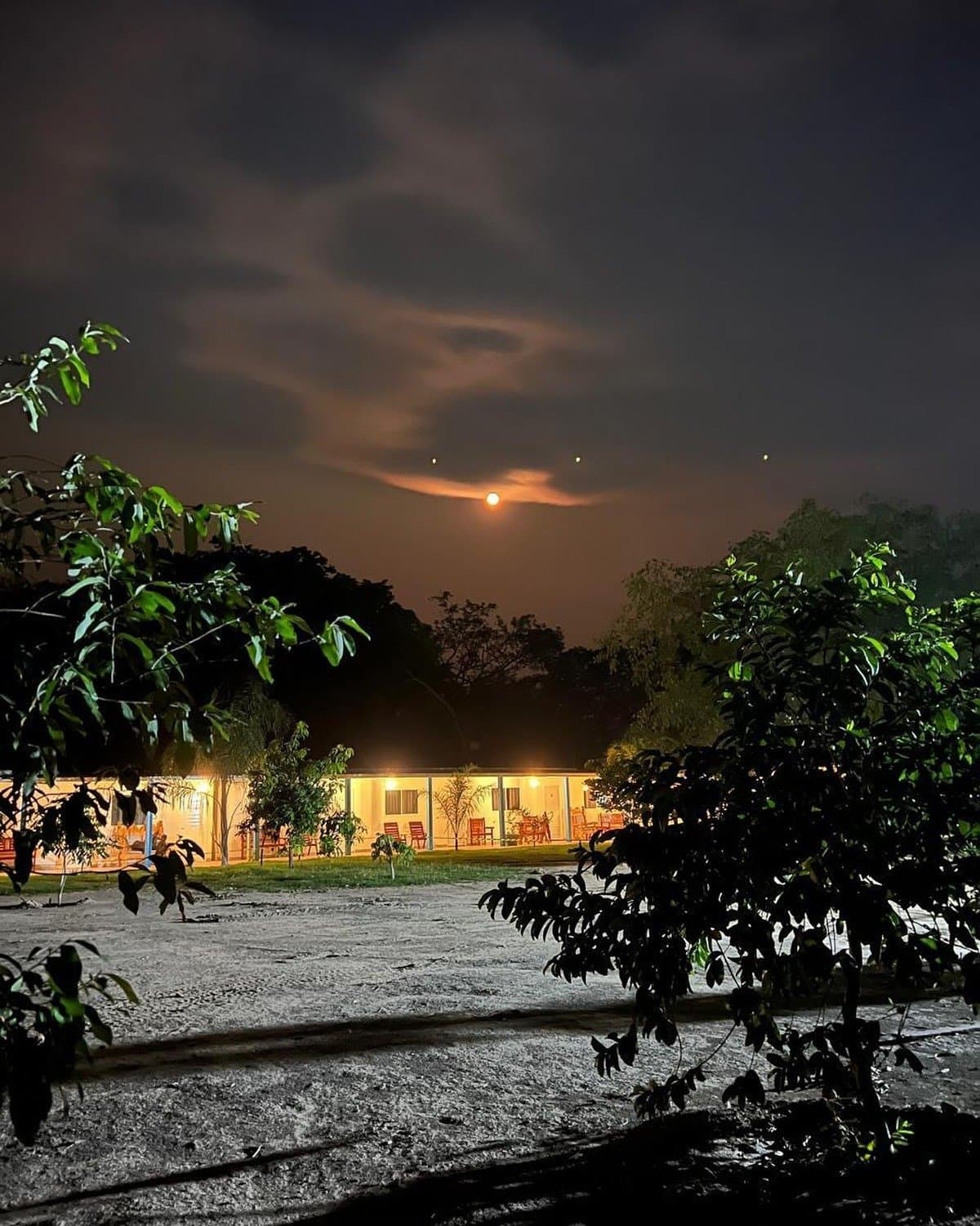 Nights at the lodge have their own quiet rhythm. A warmly lit lodge glows against a dramatic night sky on a pantanal jaguar budget safari, with a full moon rising through dark clouds above tropical trees