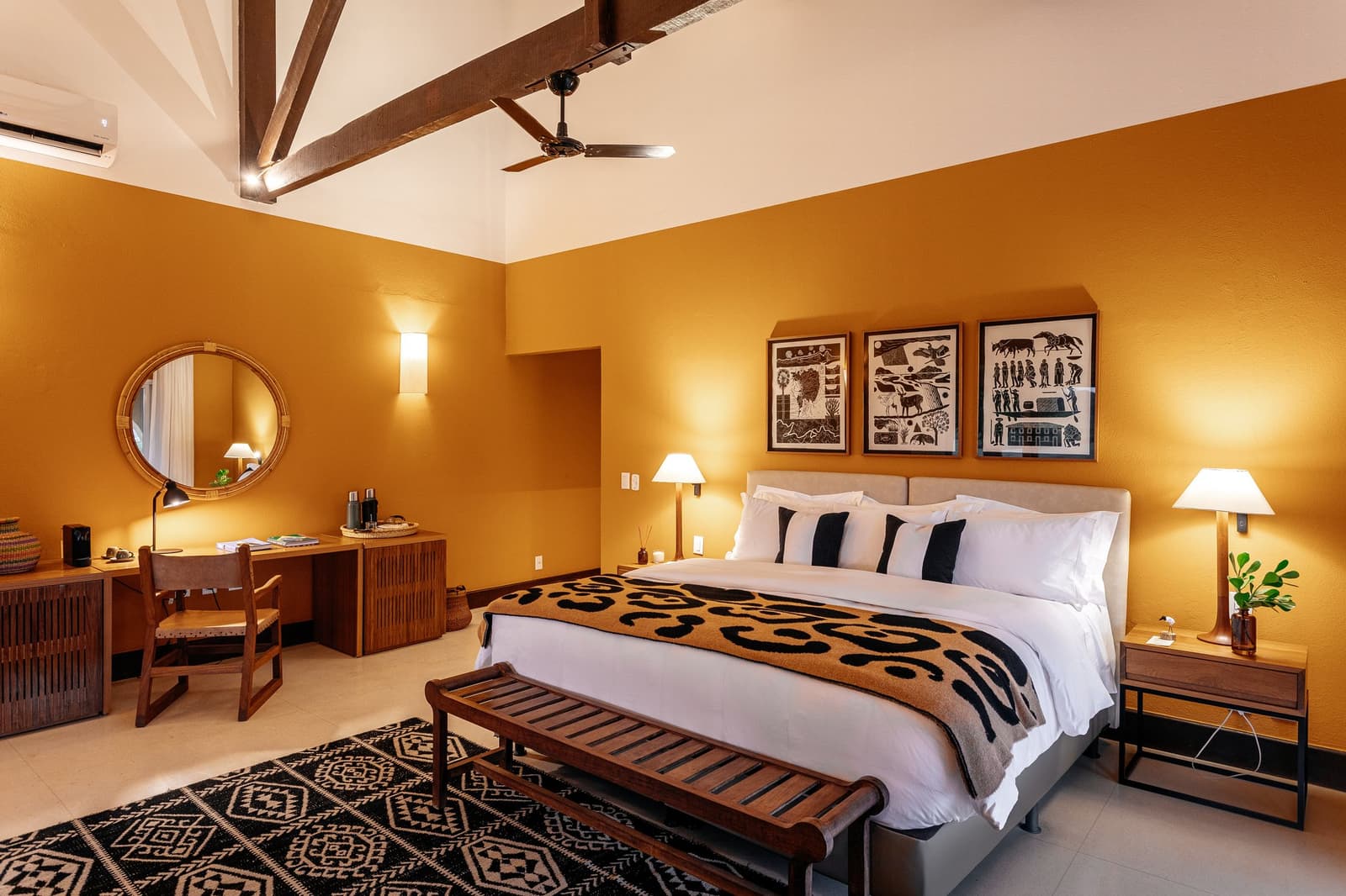 After a long day on the water, this room earns its keep. Sun-warmed ochre walls, exposed timber ceiling beams, and folk-art prints above the king bed in a pantanal luxury safari lodge room