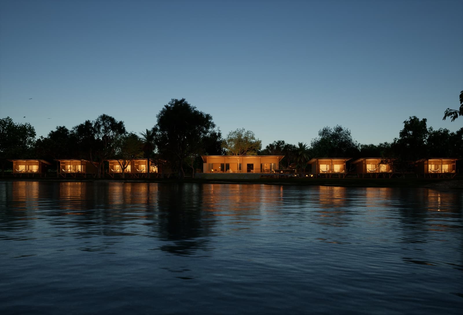 The lodge lights up at dusk, and the river keeps a perfect copy. Illuminated bungalows and a central lodge building of a pantanal luxury safari camp reflected in a calm river at dusk, framed by silhouetted trees under a deep blue twilight sky