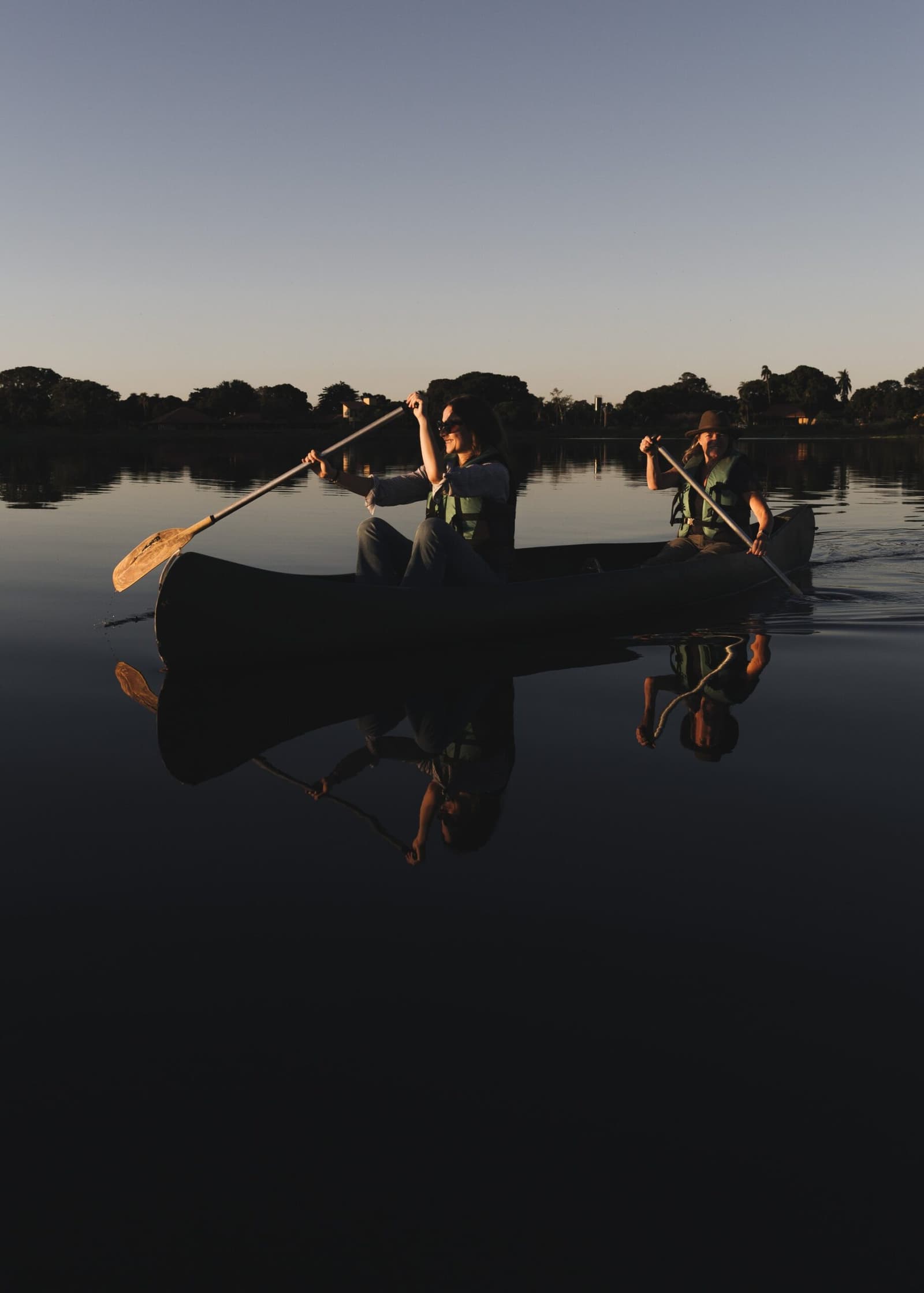 The water so still, you get two sunsets for the price of one. Two guests in life vests paddle a canoe across mirror-still water at dusk on a pantanal luxury safari, their reflections perfectly mirrored on the glassy surface