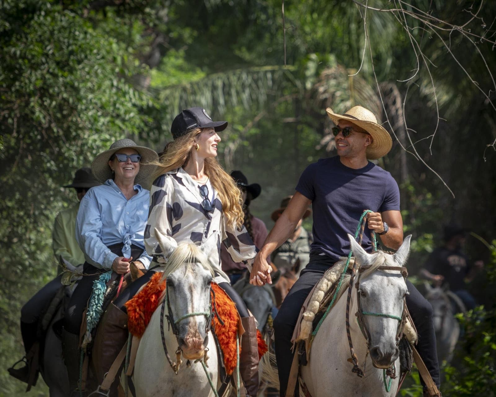 Holding hands on horseback. Not a bad way to see the Pantanal. A group of smiling riders on grey horses moves through a lush green corridor on a Pantanal Tour from Cuiabá, a couple in the foreground holding hands in the saddle