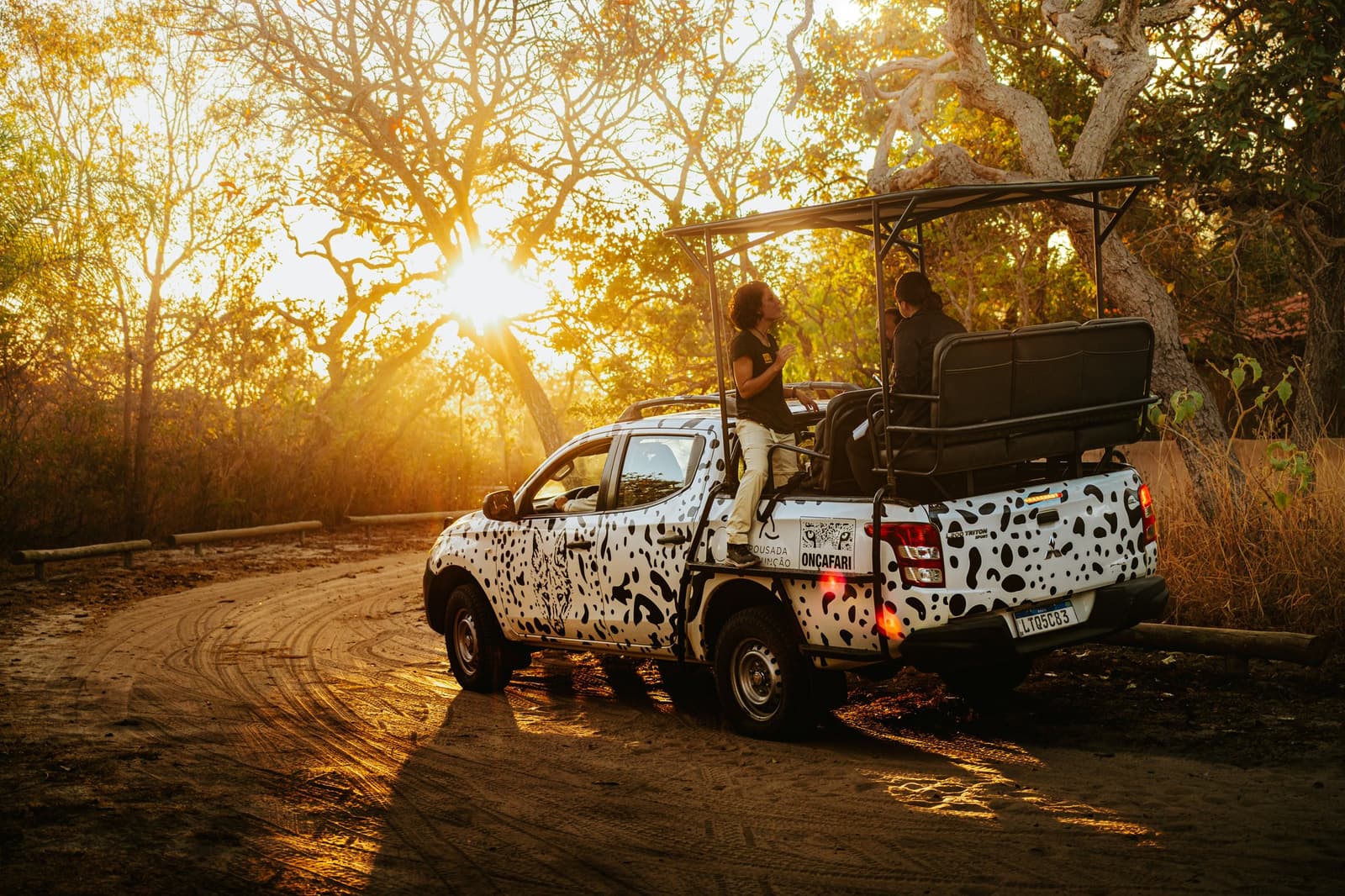 The best debriefs happen at sunset, halfway down a dusty trail. Oncafari jaguar-spotted safari truck with guests on board paused on a dirt track at golden-hour sunset in the Cerrado at Pousada Trijunção