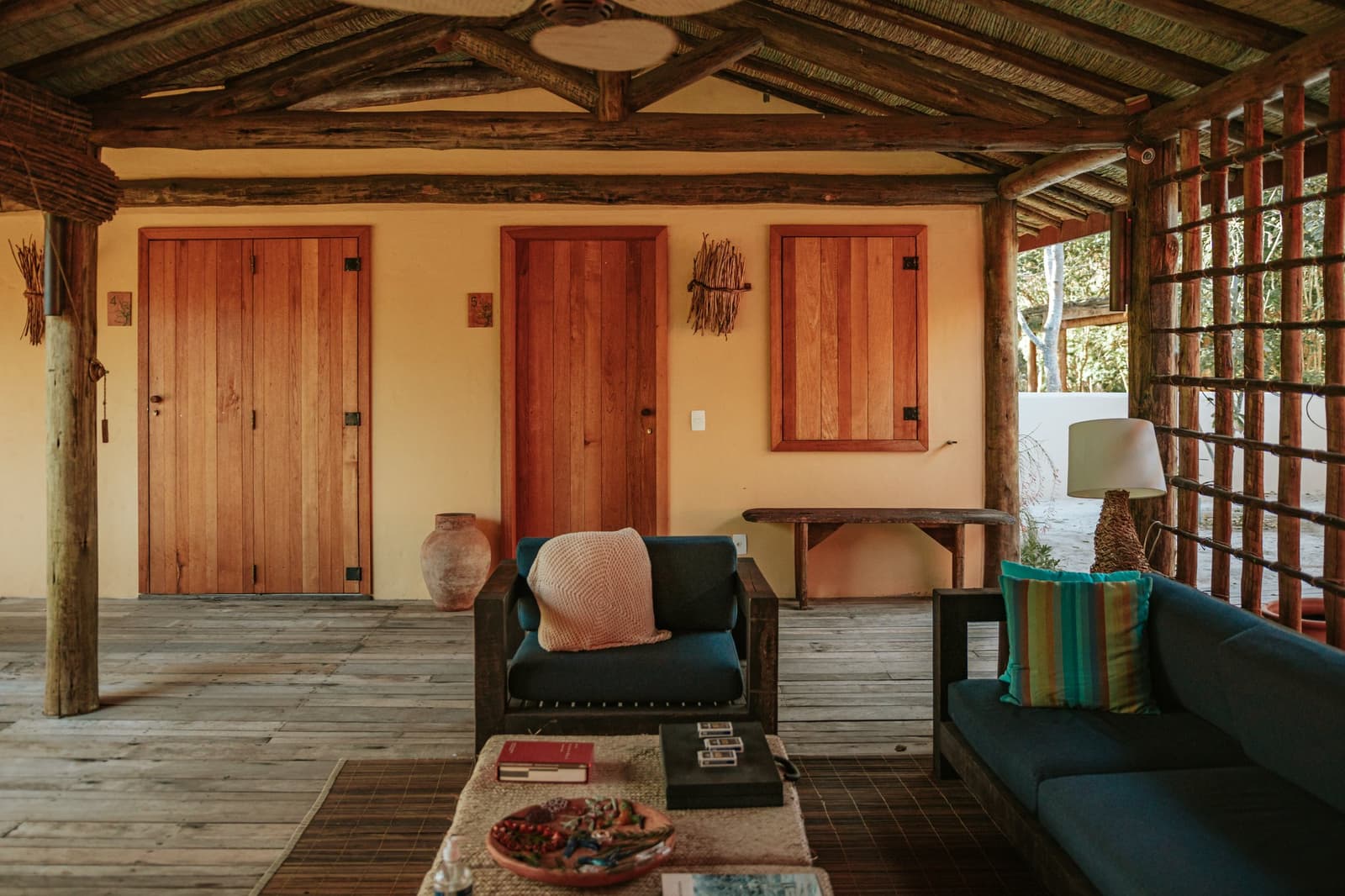 The kind of common room where you actually want to sit still for a while. Open-air covered veranda at Pousada Trijunção with teal armchairs, wooden log pillars, warm terracotta walls and handcrafted wooden doors