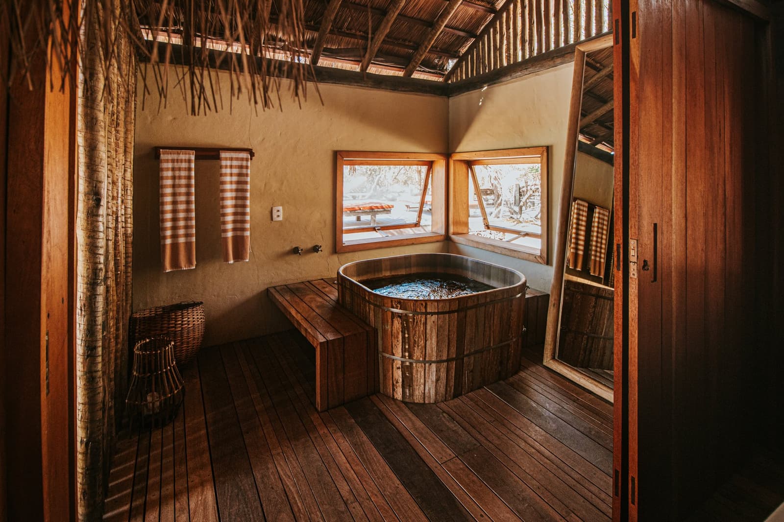 Roughed it never looked this good, a barrel bath at the edge of the wild. Rustic wooden barrel bathtub inside a Pousada Trijunção suite with thatched ceiling, warm timber floors and open windows overlooking the Cerrado landscape