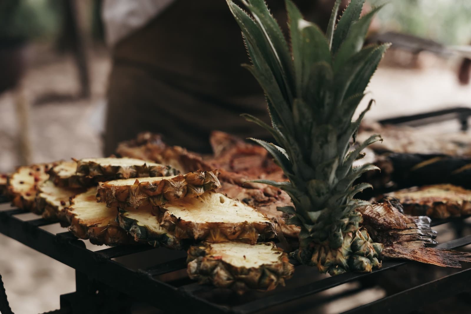 Fruit grilled over fire hits differently out here. Halved pineapple with its crown intact resting on a dark outdoor grill grate alongside caramelised slices, served during the untamed amazon cruise