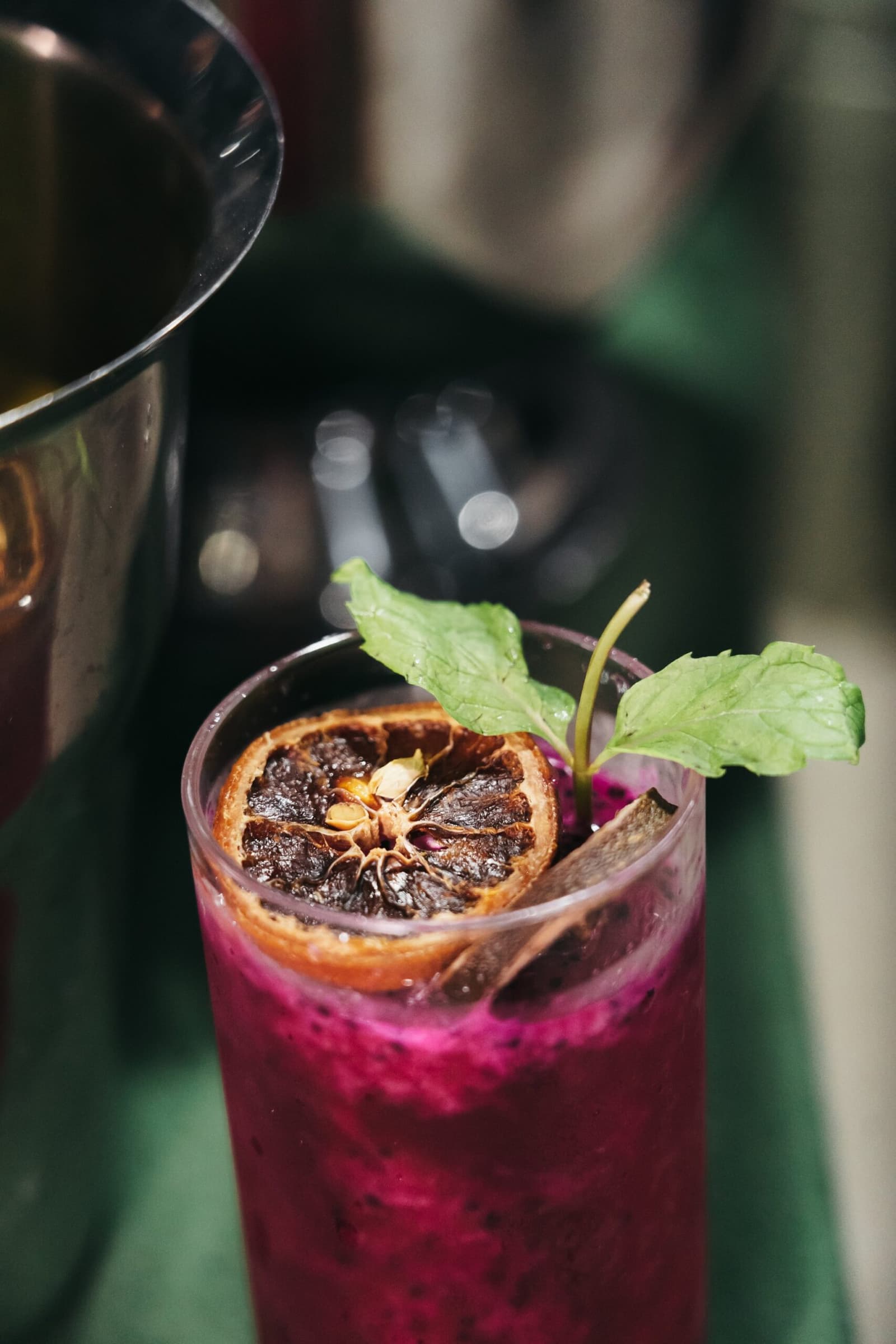 The bar team clearly did not come to play it safe. A vibrant magenta cocktail garnished with a dehydrated citrus slice and fresh mint leaves, being poured aboard the untamed amazon cruise
