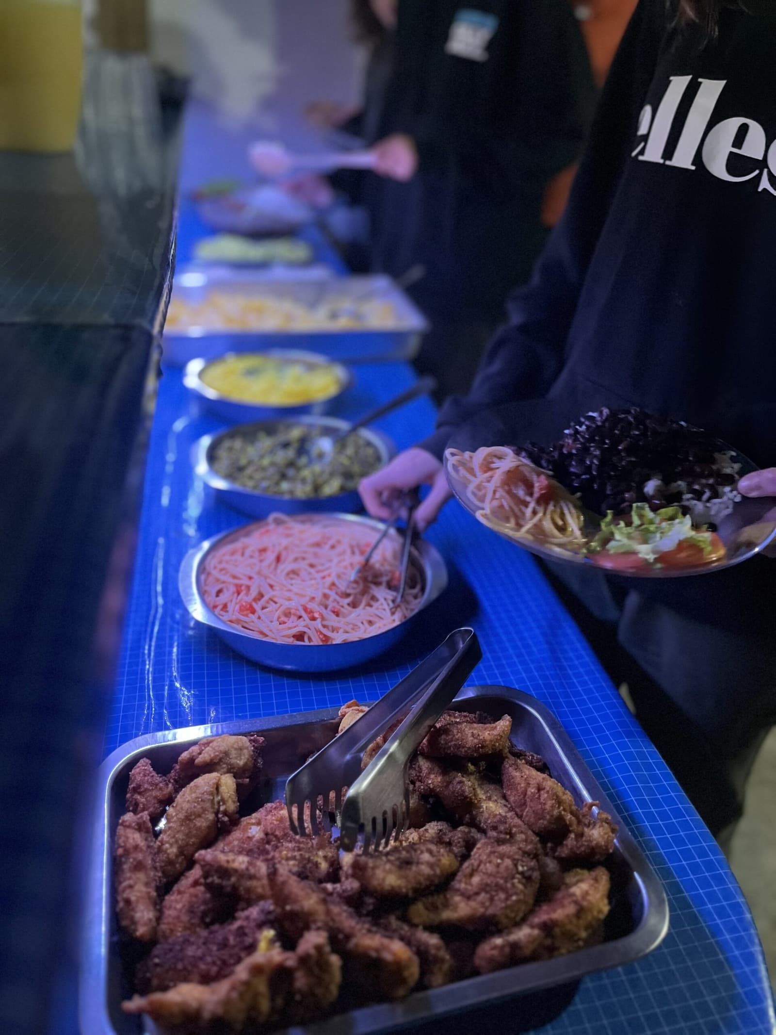 Fuel for the trail: hearty, unpretentious, and genuinely good. A long buffet line of home-cooked dishes including breaded fried meat, tomato pasta, lentils, and fresh salad served on a blue-covered table during a Vale do Pati Trek homestay dinner