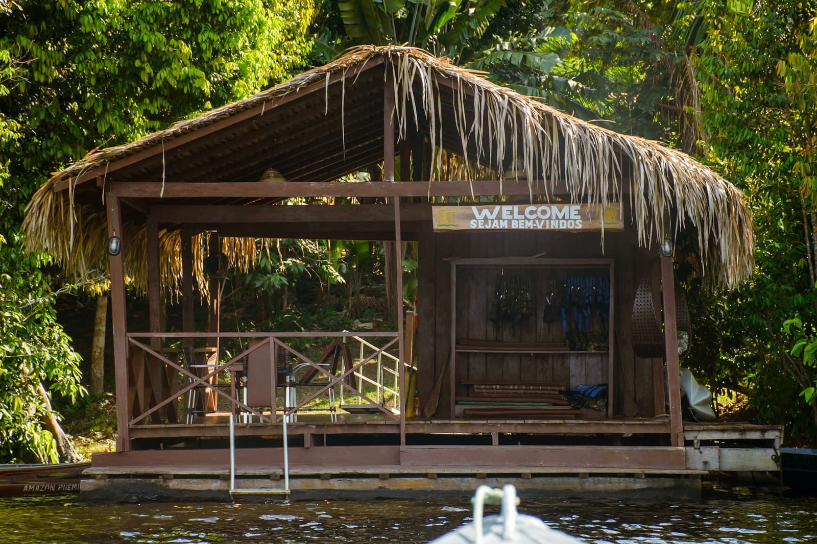 Your first view arriving by boat says everything about what comes next. A thatched-roof wooden dock pavilion with a 'Welcome / Sejam Bem-Vindos' sign, seen from the water on an amazon and pantanal tour, surrounded by dense rainforest vegetation
