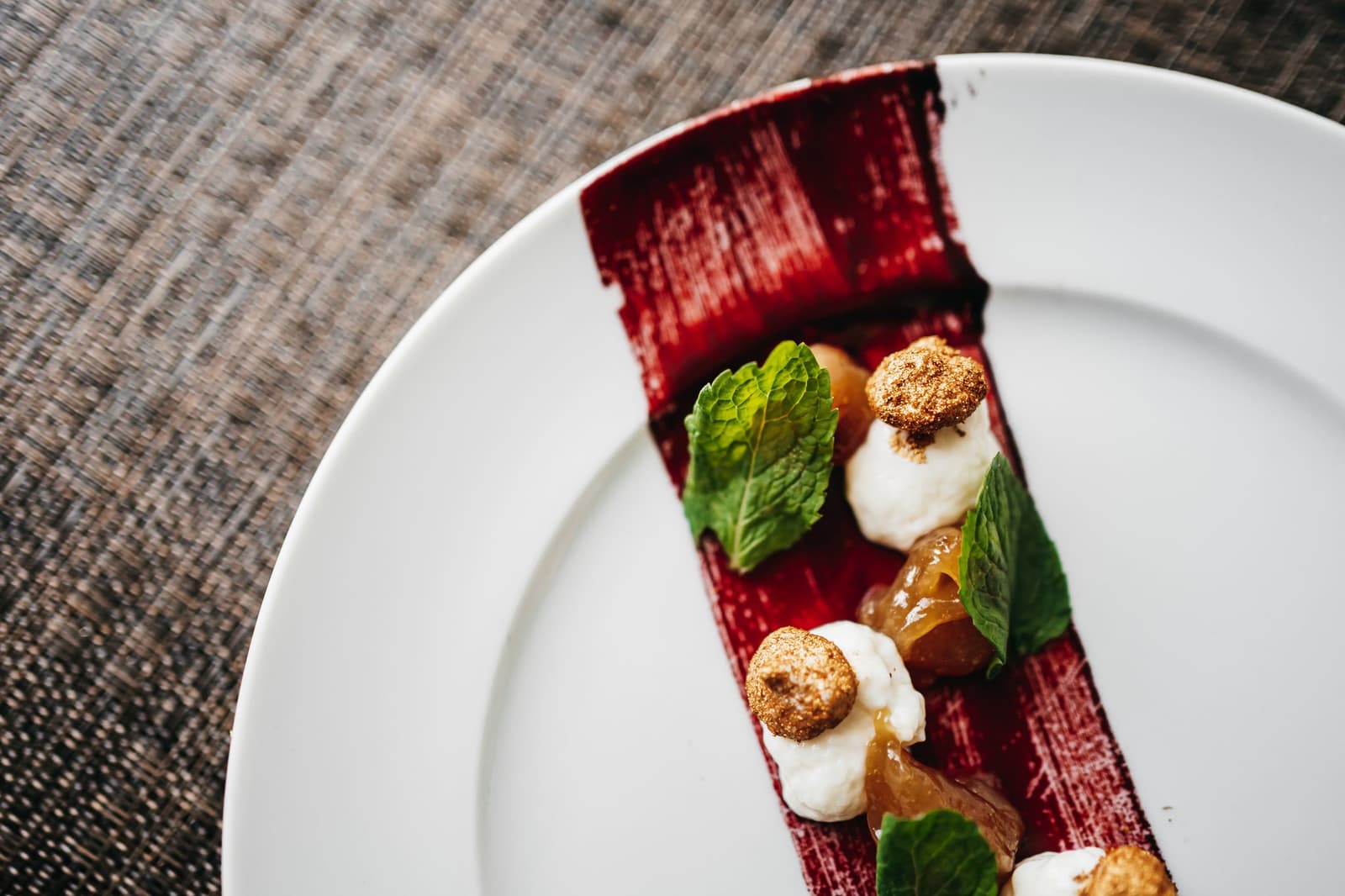 River life, it turns out, comes with a pastry chef. An elegantly plated dessert on a white round plate featuring a deep-red rectangular base topped with cream dollops, golden crumble rounds, translucent fruit pieces, and fresh mint leaves, served aboard a luxury Amazon cruise in Brazil.