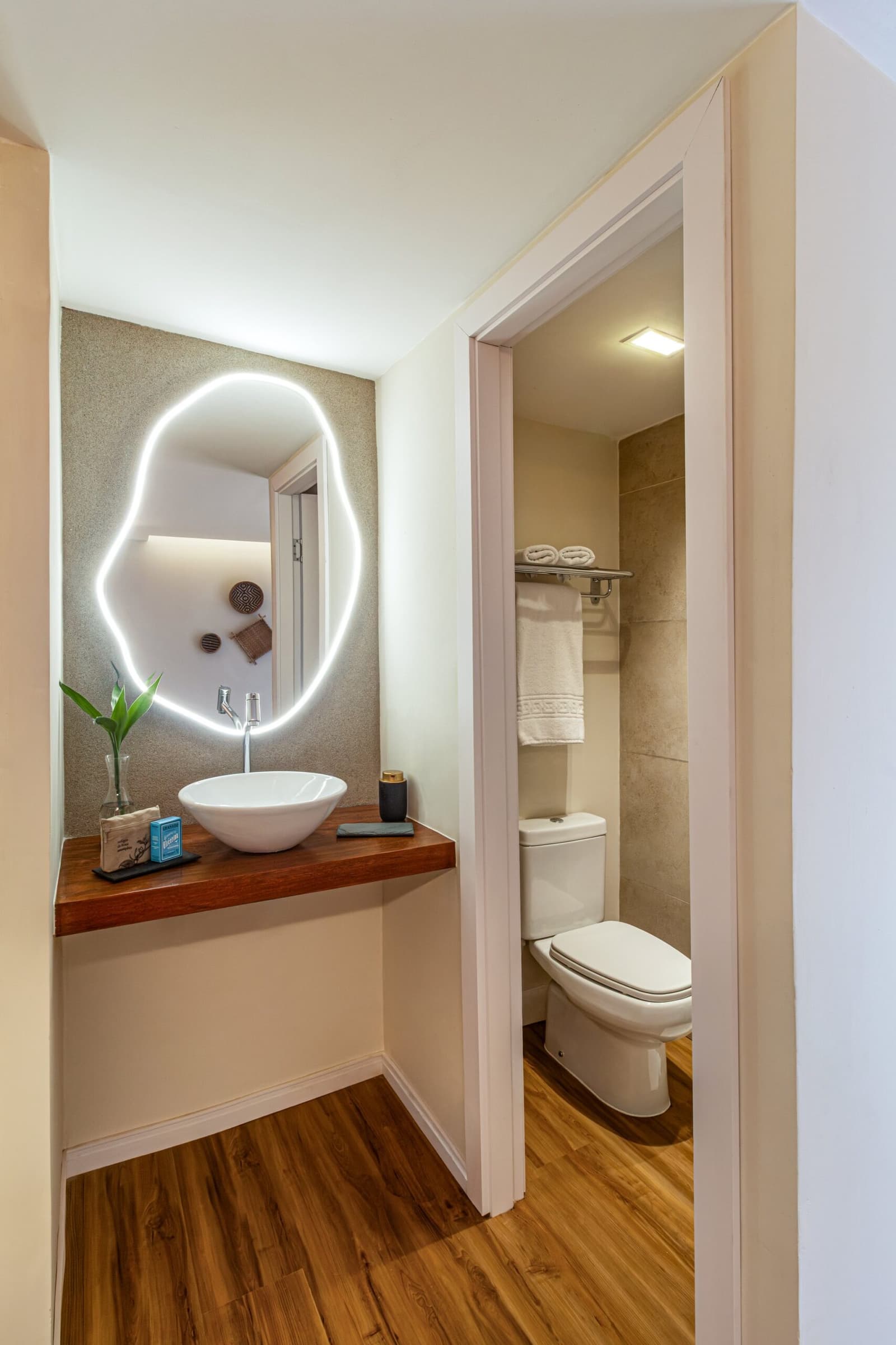 Small details done right: the kind of bathroom that earns its own review. Photo: STUDIO CREATE Private en-suite bathroom on a luxury Amazon cruise in Brazil, featuring a bowl sink on a warm wood countertop, an organic-shaped LED backlit mirror, and a separate toilet area with rolled towels and stone-effect wall tiles