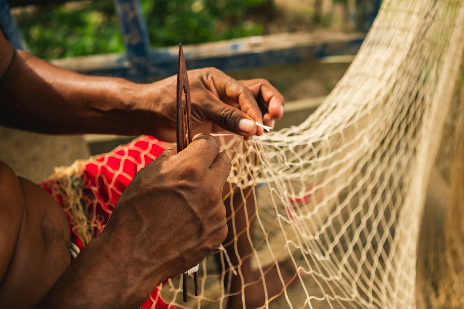 Knot by knot, the river gives back what it takes. Photo: Guilherme Gomes Close-up of a person's hands mending a fishing net with a wooden needle during a riverside community visit on an amazon rainforest ecolodge trip in brazil