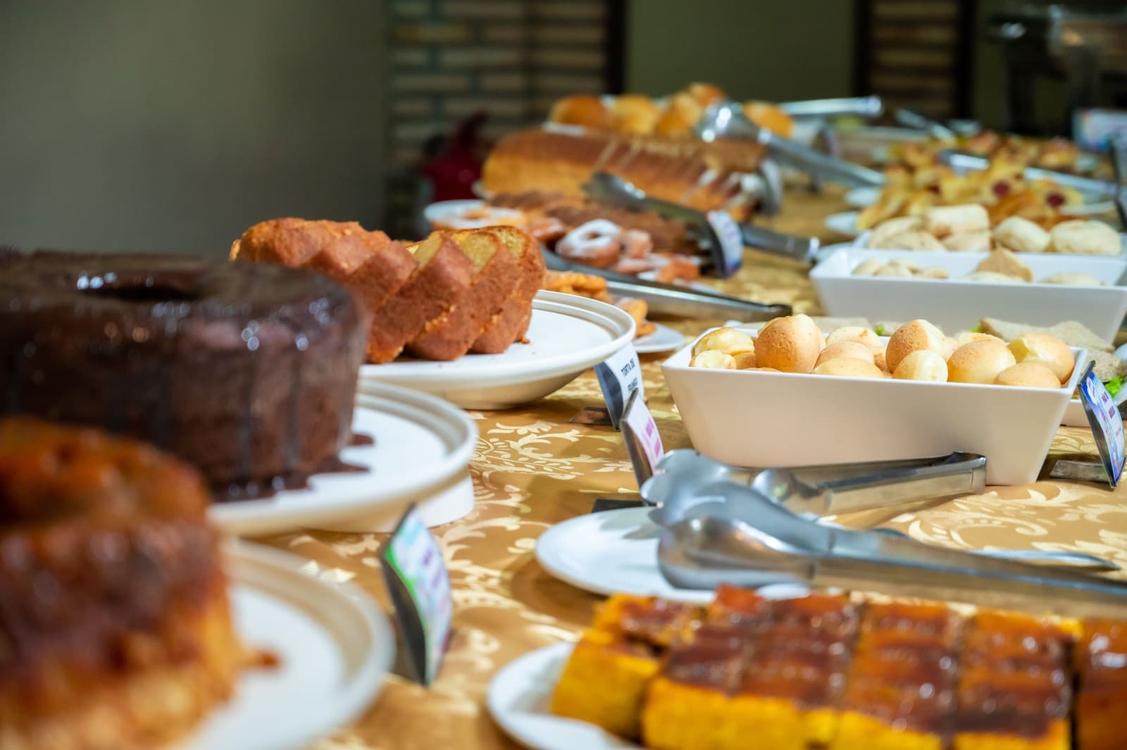 Carb-loading before jaguars is not just allowed, it is strongly encouraged. A long buffet table on an amazon and pantanal tour loaded with sliced pound cakes, pão de queijo, sweet rolls, pastries, and glazed sweets on a gold-patterned tablecloth