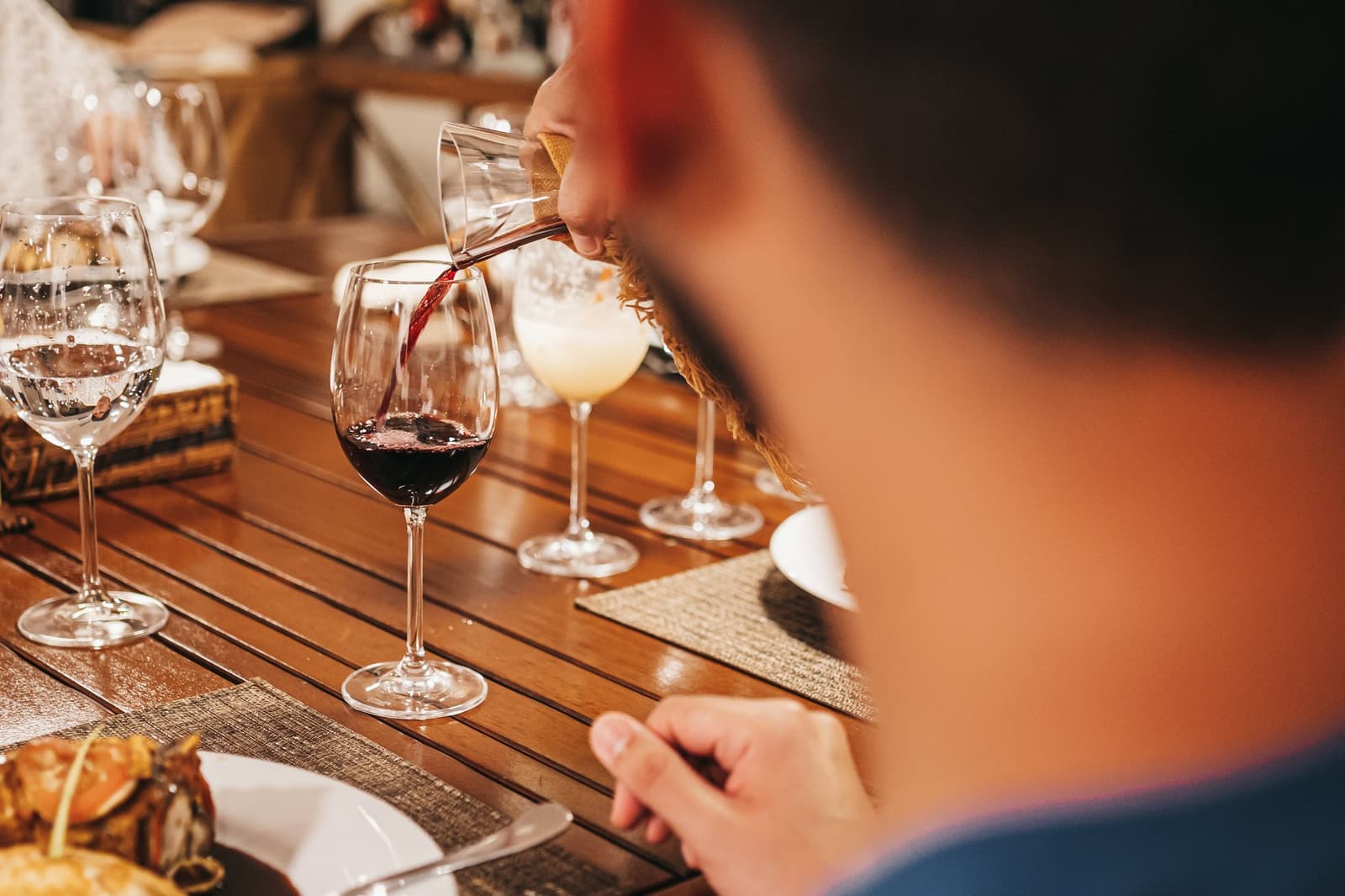 Wine poured, table set, river somewhere out there doing its thing. Red wine being poured into a glass at a formally set dinner table on a luxury Amazon cruise in Brazil, with water glasses, a cocktail, and plated food visible