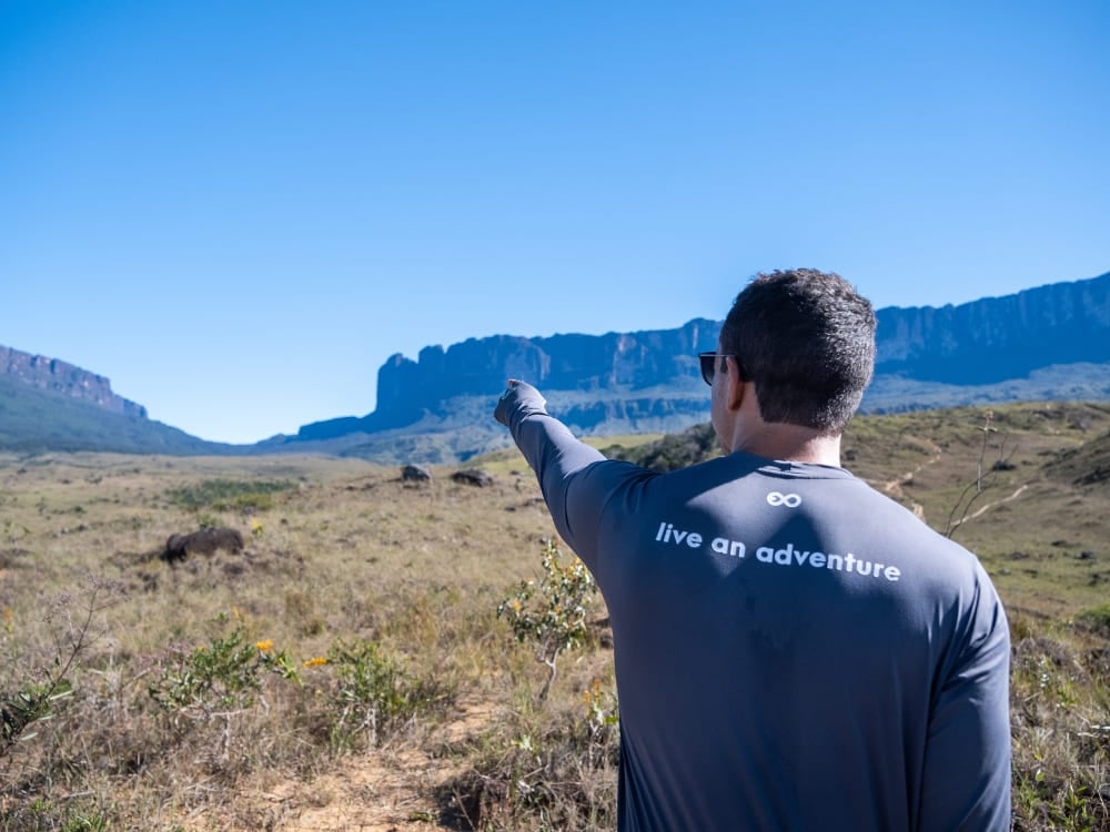 A hiker pointing toward the Kukenán tepui view from Mount Roraima A hiker pointing toward the Kukenán tepui view from Mount Roraima
