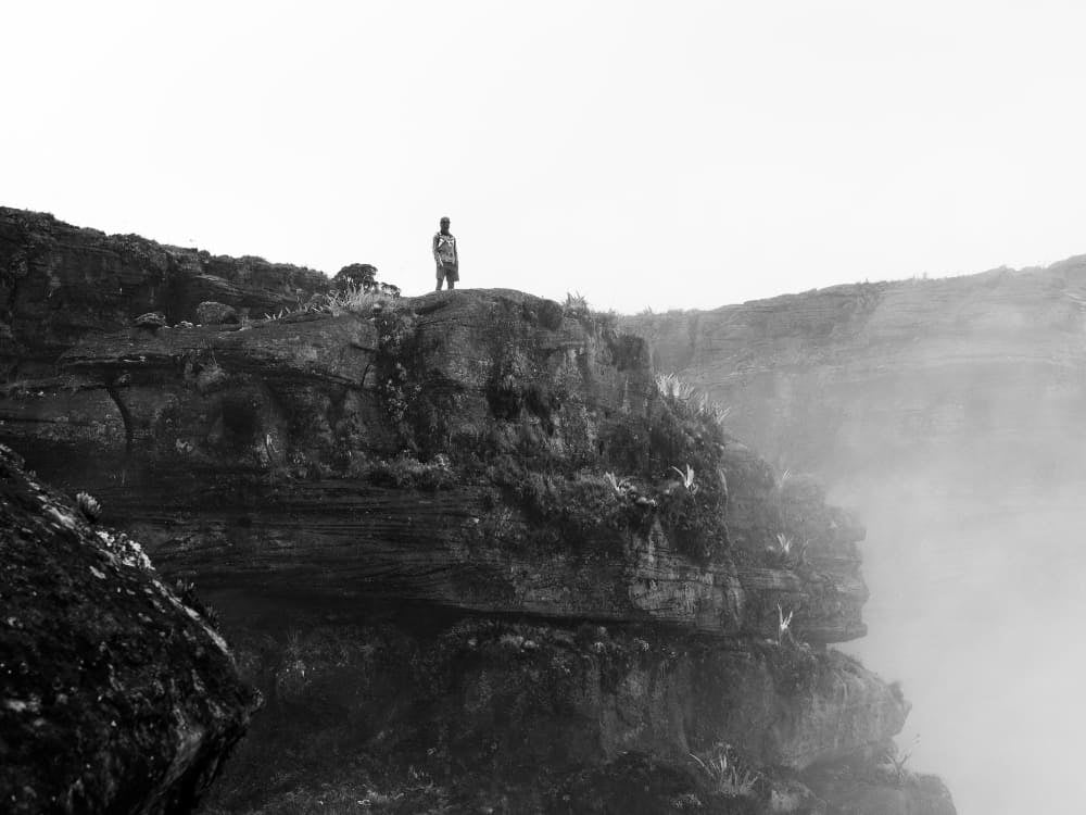 A hiker on a misty cliff at the summit of Mount Roraima, in black and white A hiker on a misty cliff at the summit of Mount Roraima, in black and white