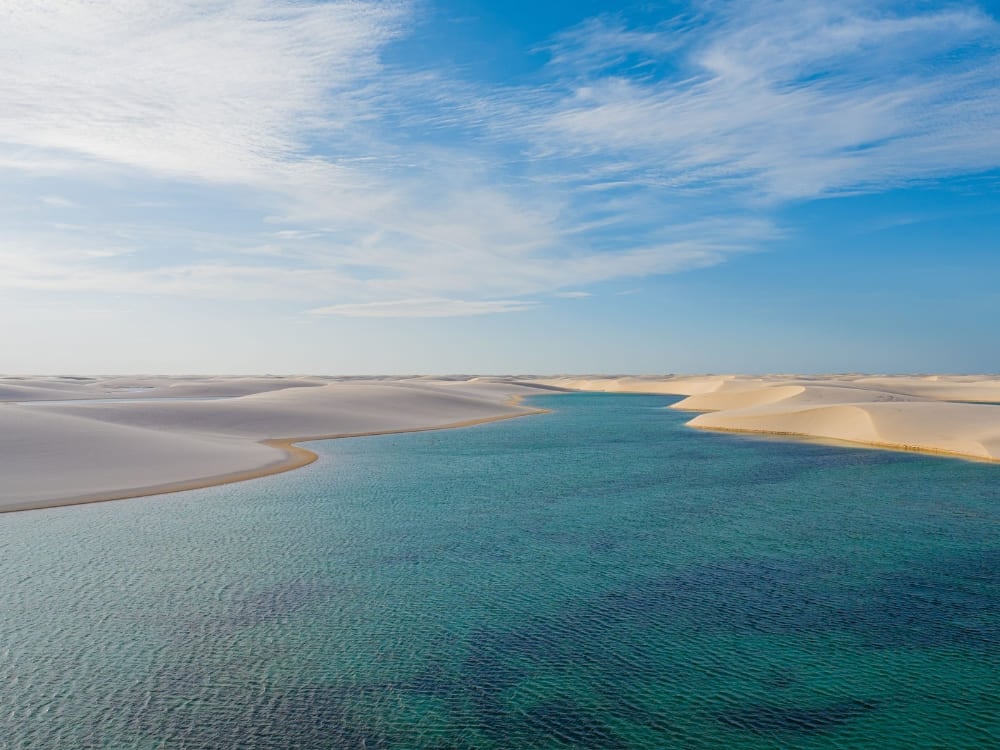 Turquoise lagoon stretching between the white sand dunes of Lençóis Maranhenses under a blue sky. Turquoise lagoon stretching between the white sand dunes of Lençóis Maranhenses under a blue sky.