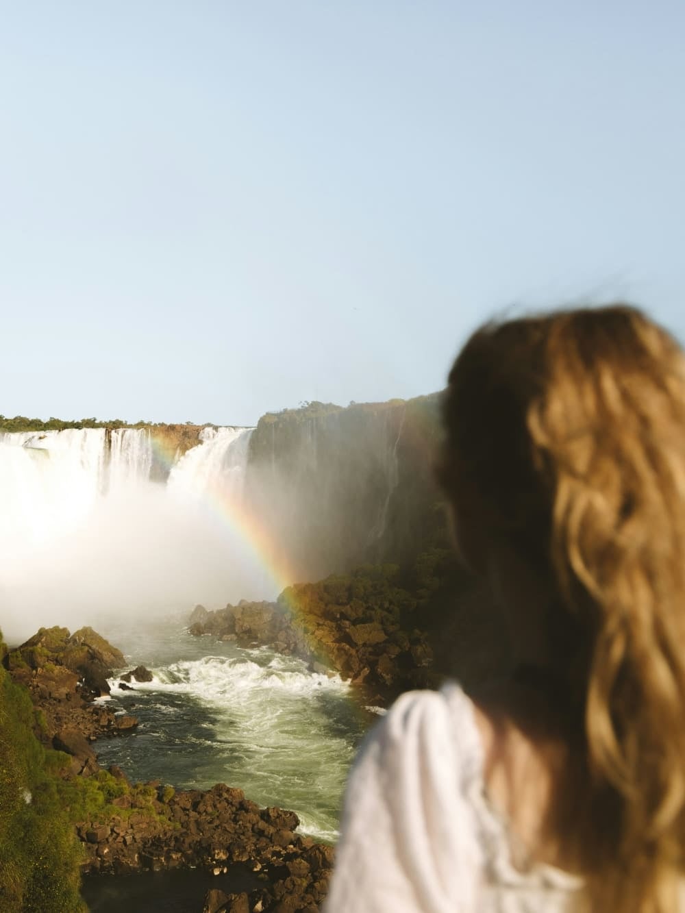 A woman looking at Iguazu Falls with a rainbow forming in the spray, Brazil. A woman looking at Iguazu Falls with a rainbow forming in the spray, Brazil.