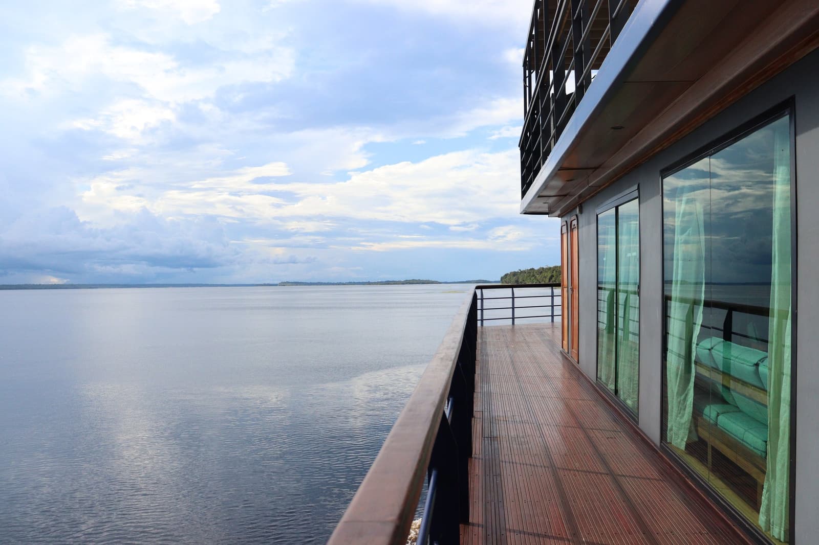 That view does not require a filter, or any effort at all. The teak side deck of the La Jangada amazon cruise stretches alongside floor-to-ceiling cabin windows, overlooking a wide, calm river with a forested island on the distant horizon