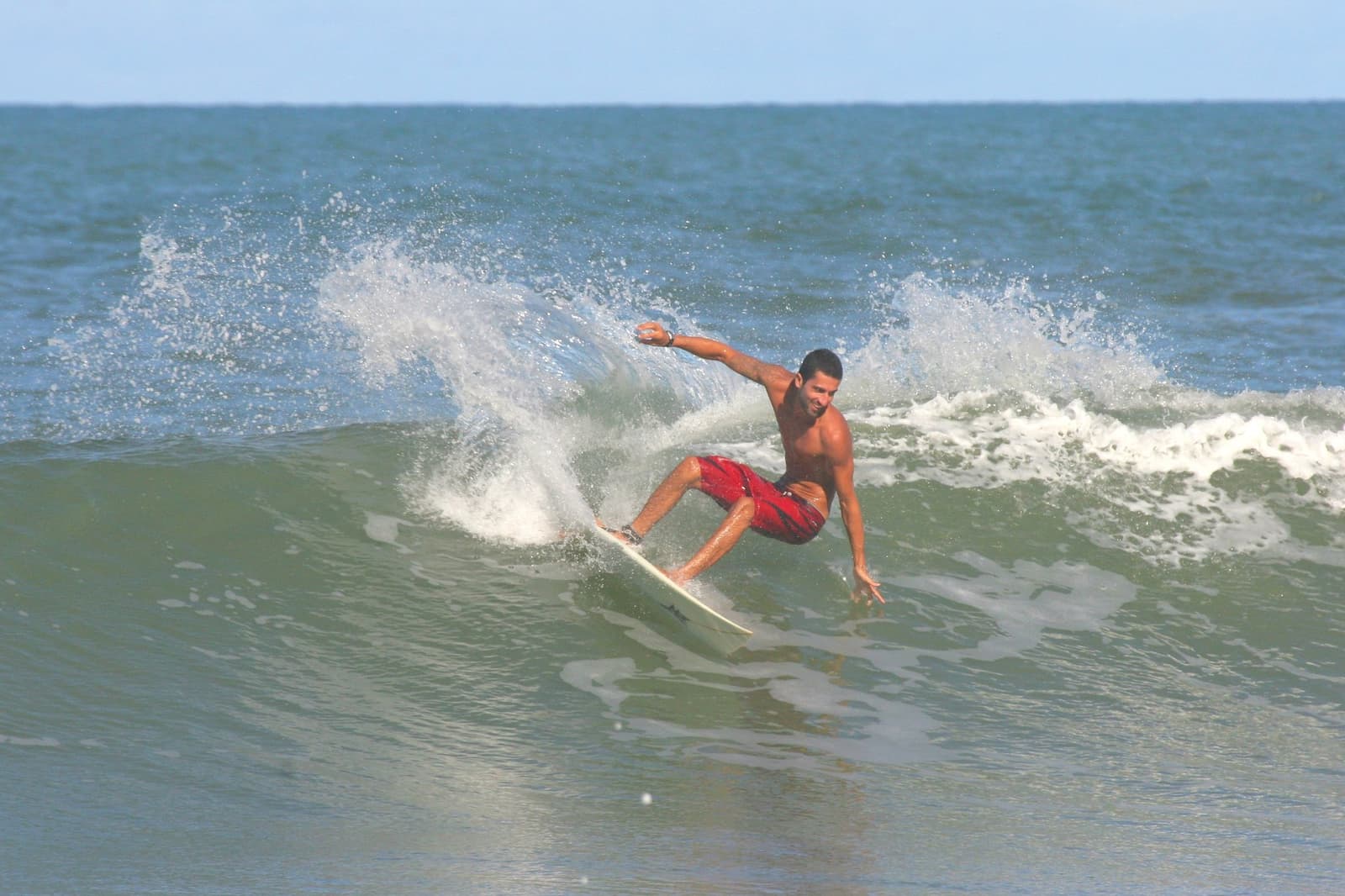 That cutback took four days of work to look that easy. Photo: Picasa A surfer in red board shorts executes a sharp cutback on a green wave at an itacaré surf school session, arms spread wide for balance as white spray fans out behind him