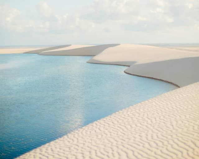 Blue rainwater lagoons between white dunes rippled by the wind in Lençóis Maranhenses National Park.