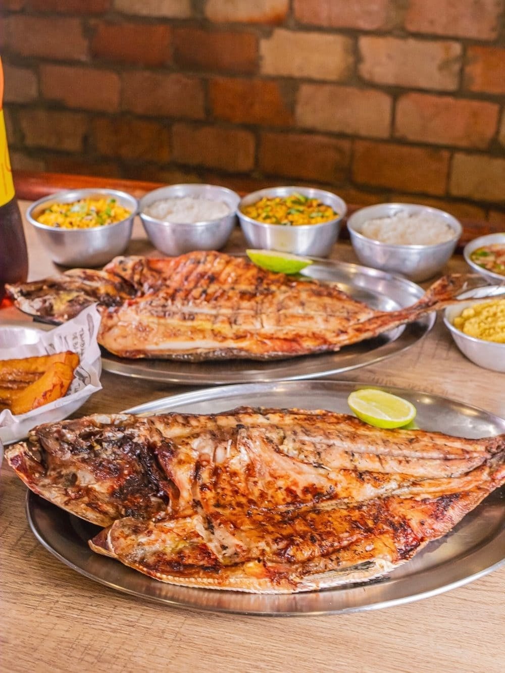@tambaquidebanda Two whole tambaqui grilled and split open on metal platters, served with lime, rice and farofa